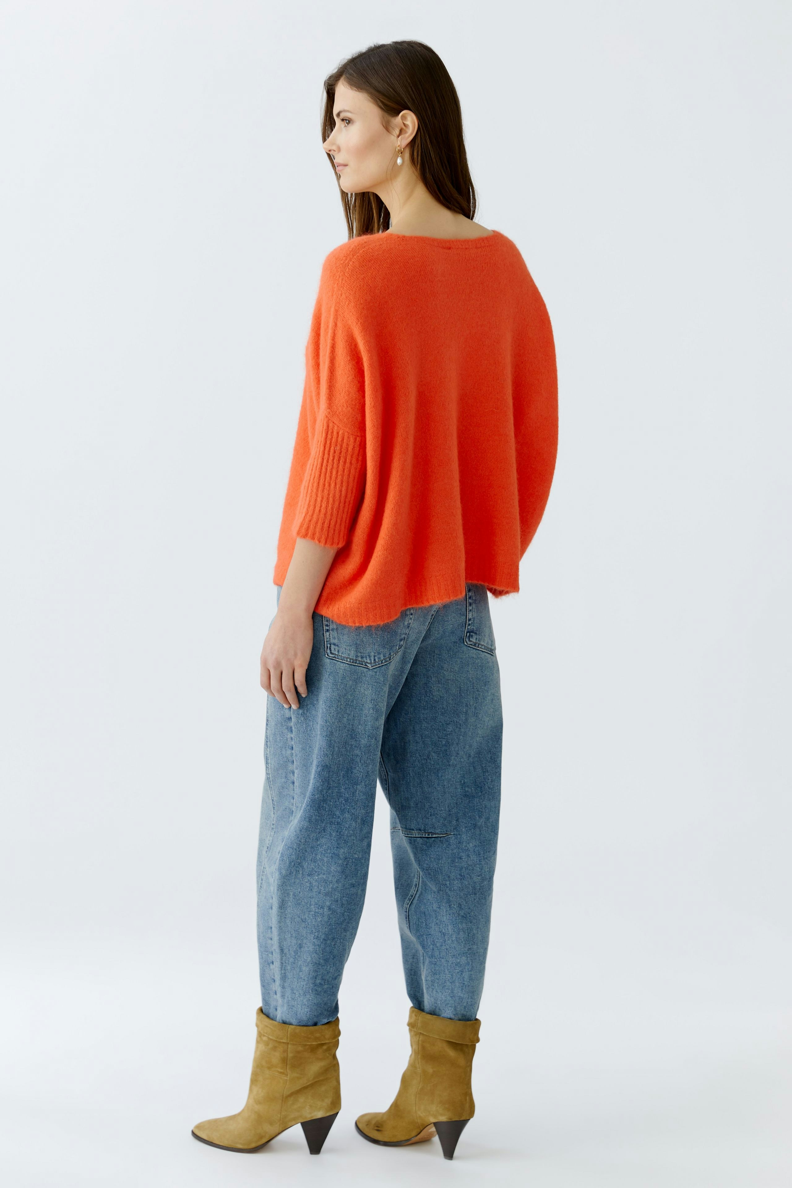 Casual women's pullover: A woman in an oversized orange pullover paired with relaxed jeans.