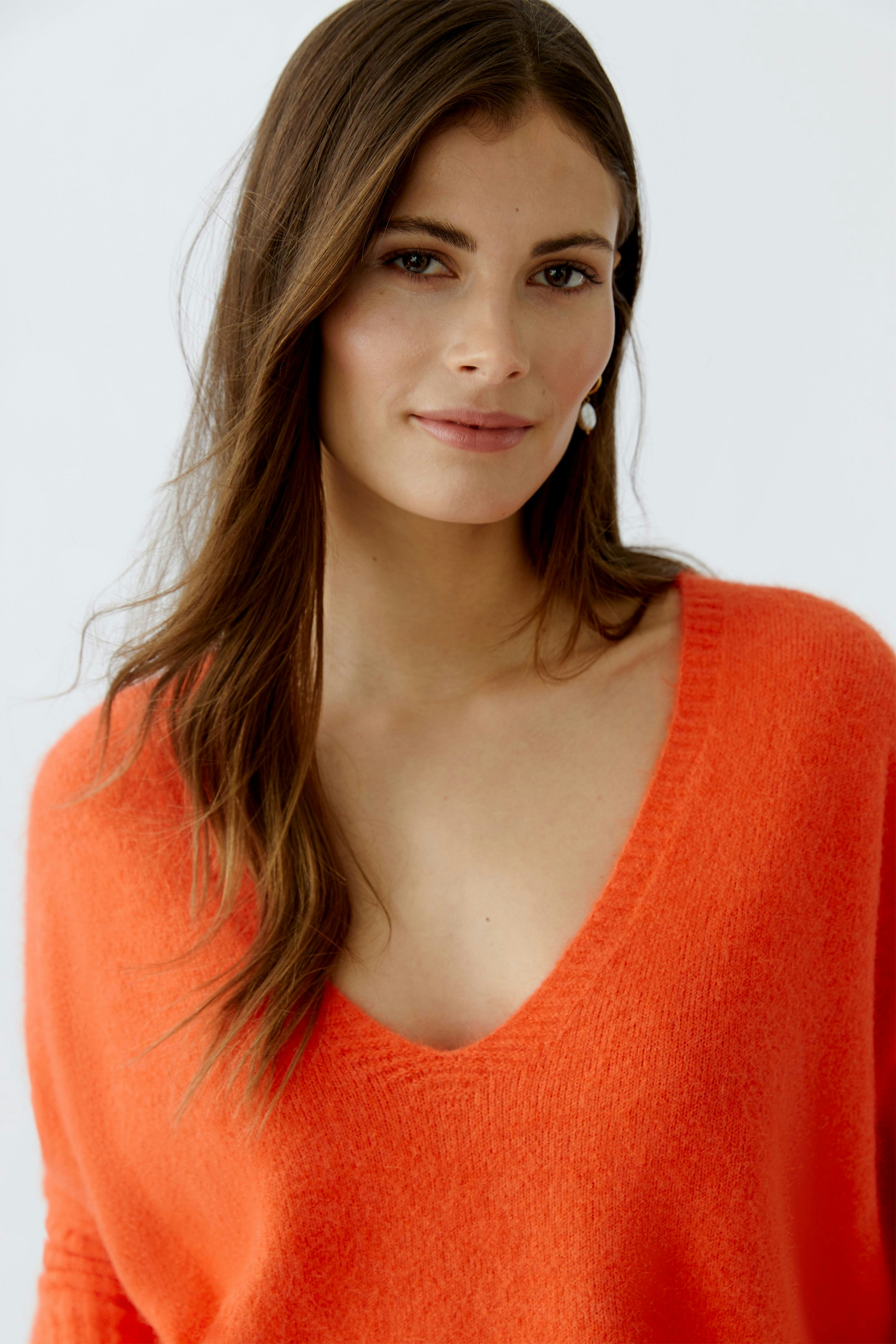 Casual women's pullover: A woman in a vibrant orange pullover with a deep V-neckline smiles confidently.