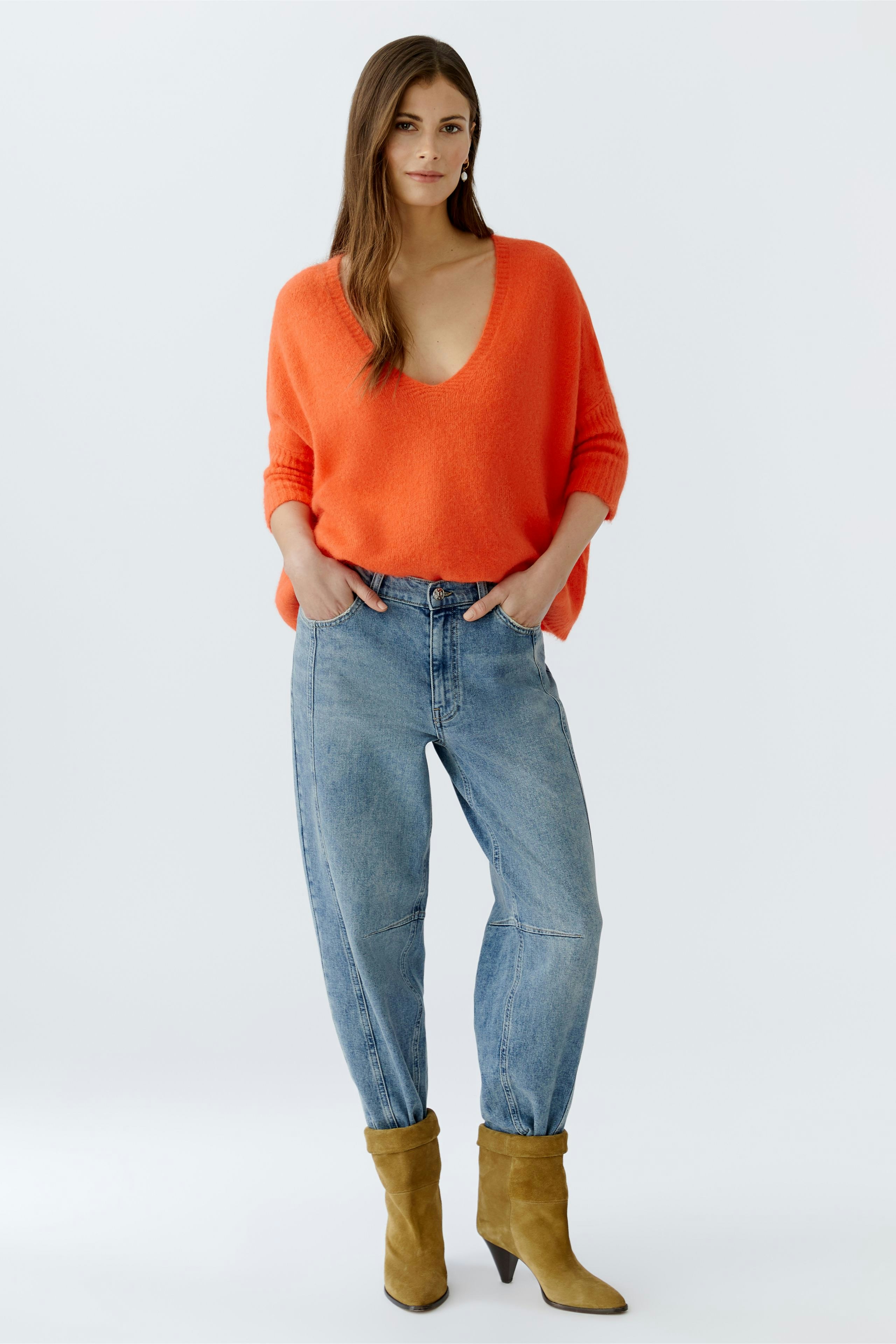 Casual women's pullover: Young woman in an orange oversized pullover paired with blue jeans.