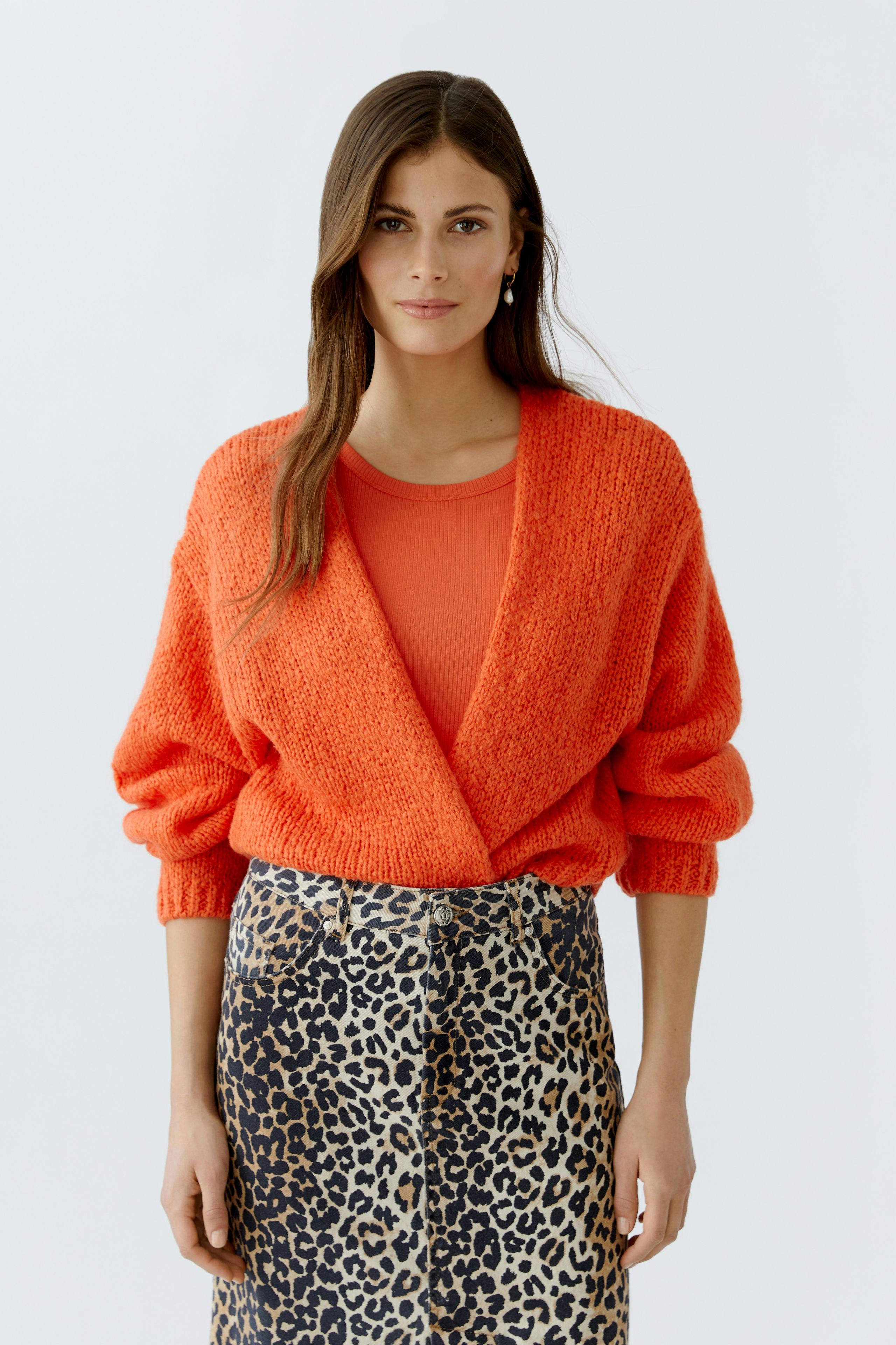 Modische Damen-Strickjacke: Frau in leuchtend orangefarbener Strickjacke mit lässigem Look.