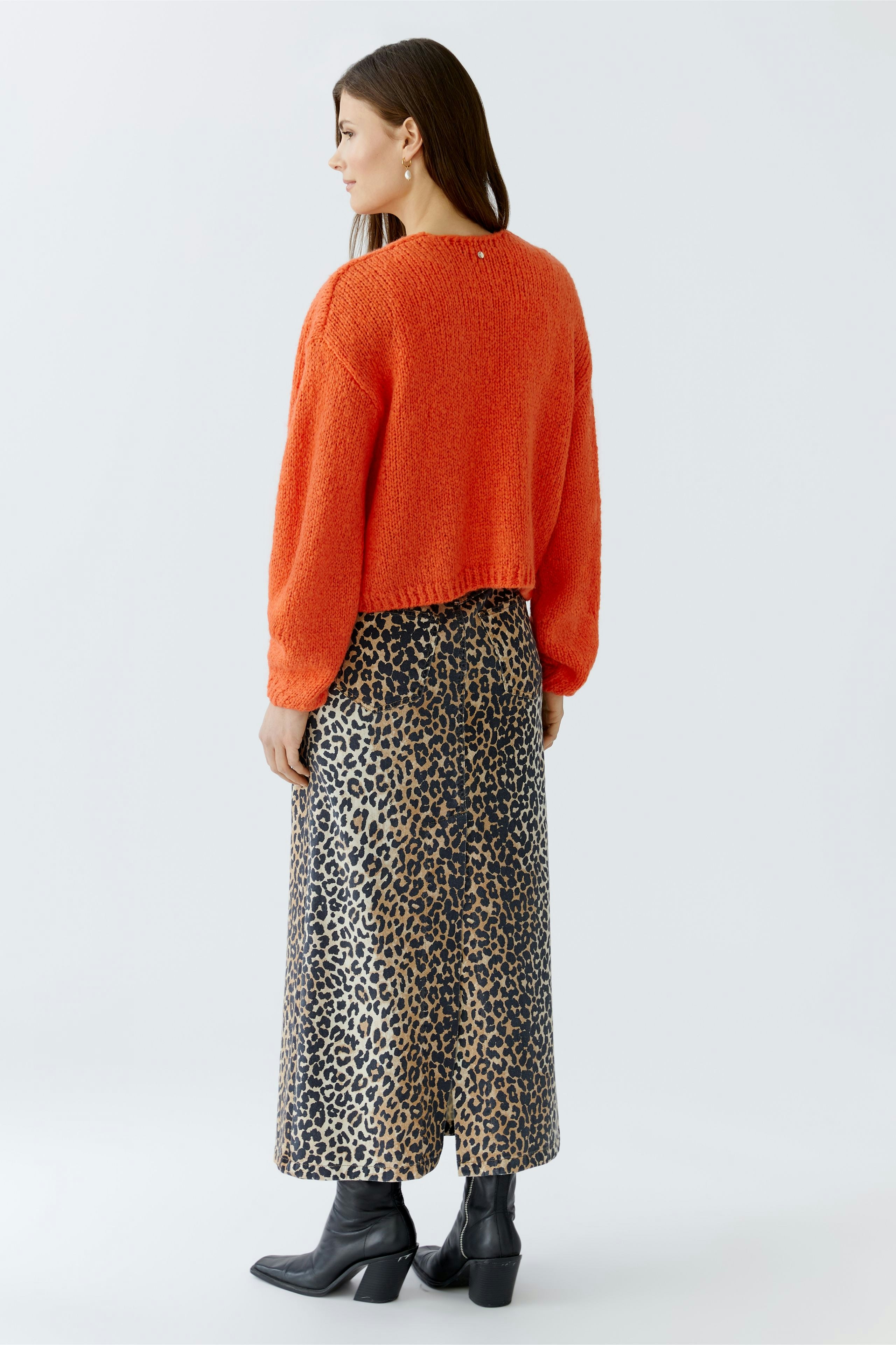 Damen-Strickjacke: Frau in orangefarbener Strickjacke mit lässigem, gemustertem Rock von hinten.