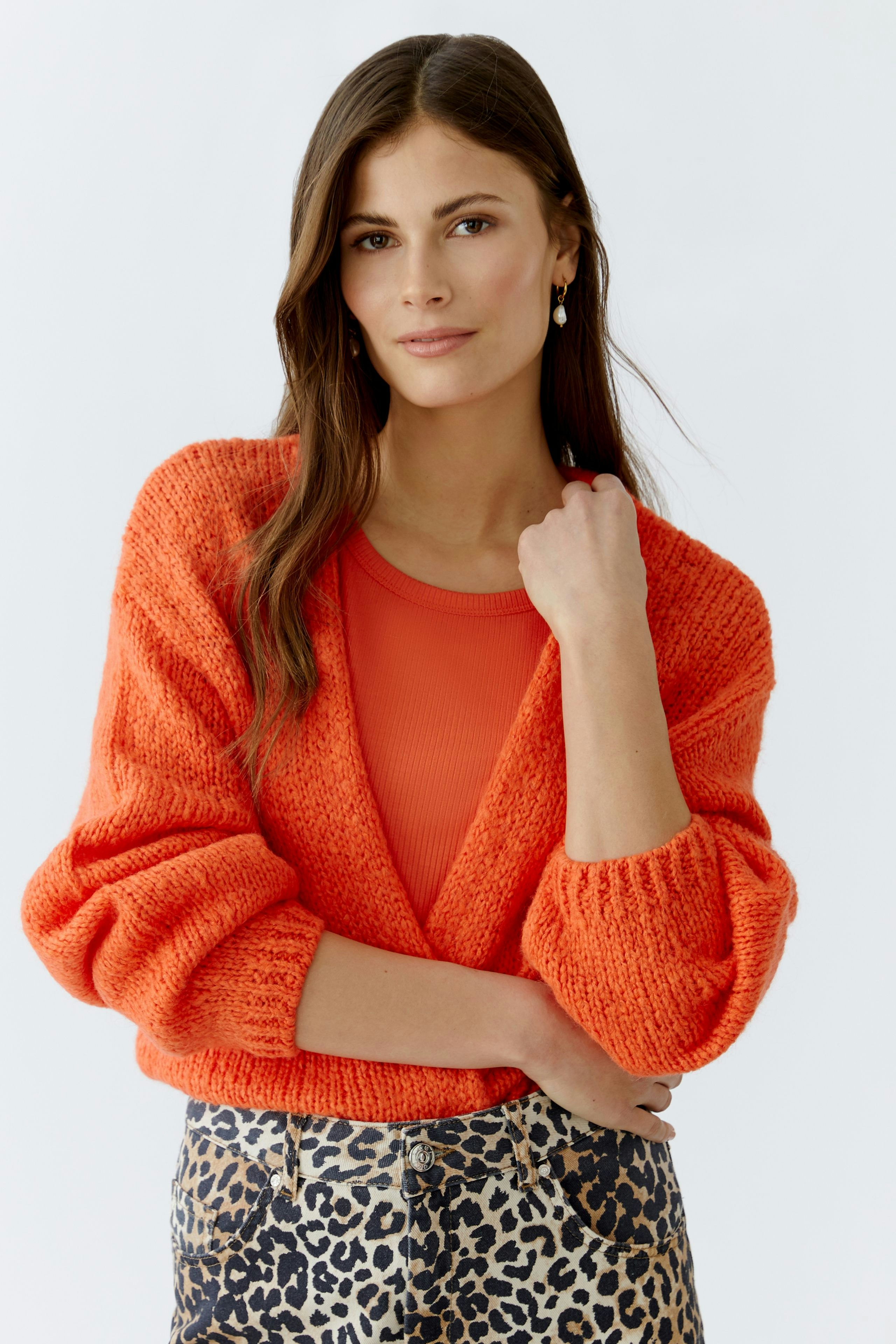 Bequeme Damen-Strickjacke in leuchtendem Orange, lässig kombiniert mit einem roten Top und einem gemusterten Rock.