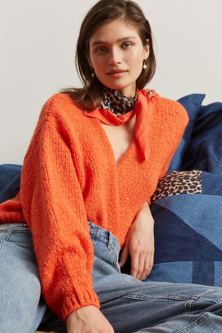 Damen-Strickjacke: Junge Frau in orangefarbener Strickjacke mit V-Ausschnitt und lässigem Look.