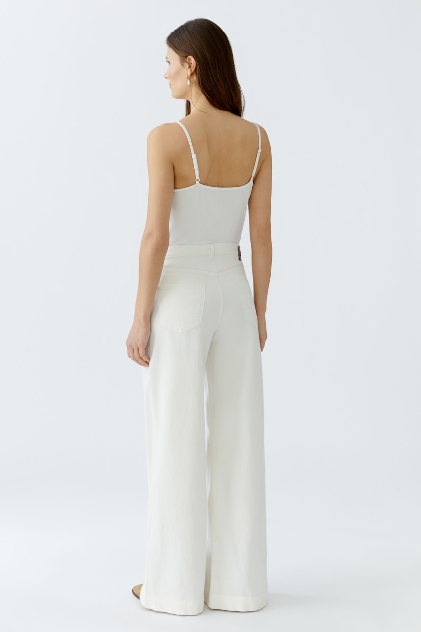 Flared jeans: A woman in white flared jeans and a simple tank top, showcasing a relaxed fit.