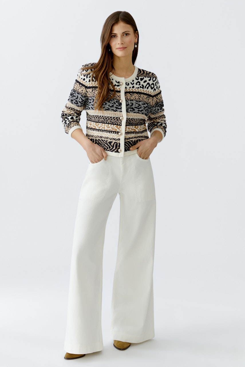 Flared jeans: Woman in stylish flared jeans paired with a patterned cardigan, hands in pockets.