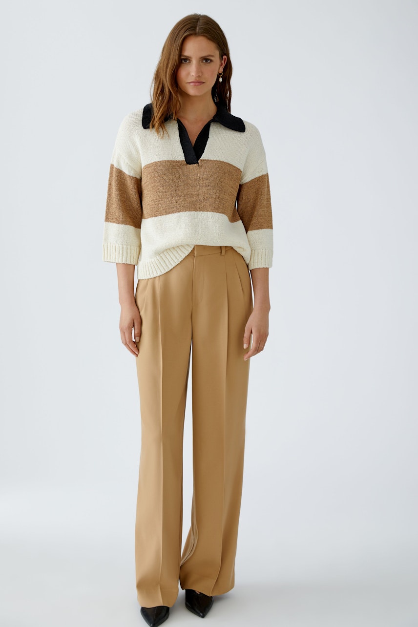 Chic women's pleated trousers: A woman in beige trousers paired with a striped pullover.