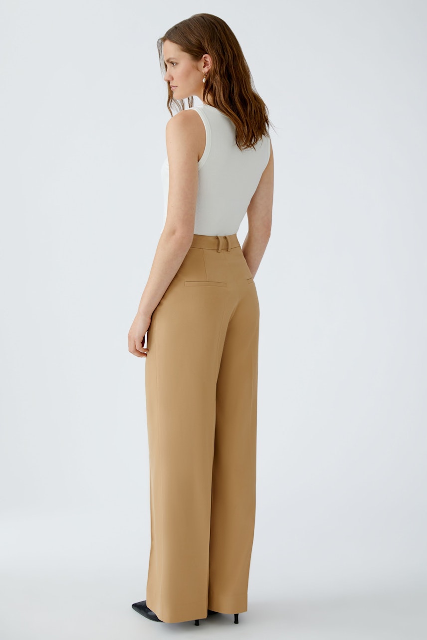 Modern wide-leg trousers: Woman in beige pleated pants, showcasing a relaxed fit and stylish design.