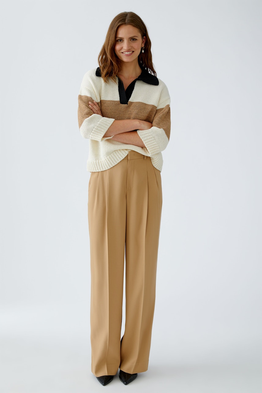 Chic women's pleated trousers: A woman in beige trousers and a striped pullover stands confidently.