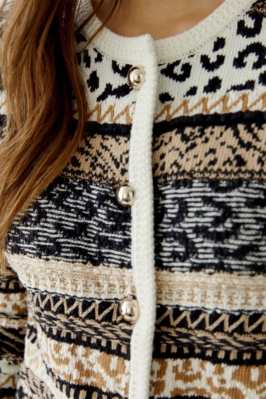 Gemusterte Damen-Strickjacke: Frau mit braun-beiger Strickjacke mit Knöpfen und grafischem Muster.