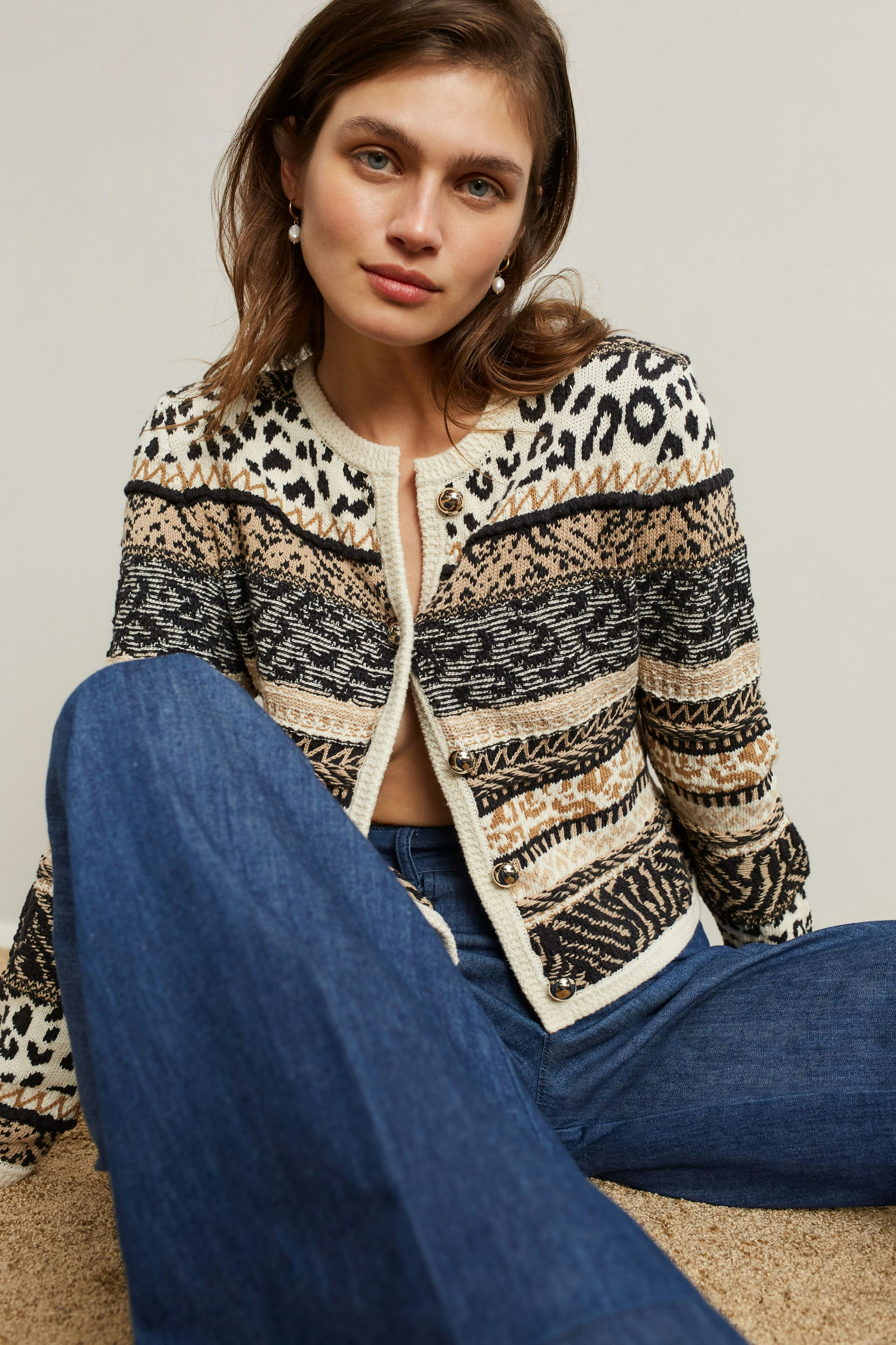 Casual women's cardigan: Young woman in a patterned knit cardigan with blue jeans, sitting comfortably.
