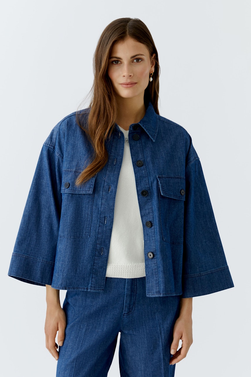 Damen-Jeansjacke: Frau in blauer Jeansjacke mit lässigem Schnitt und weißen Pullover.