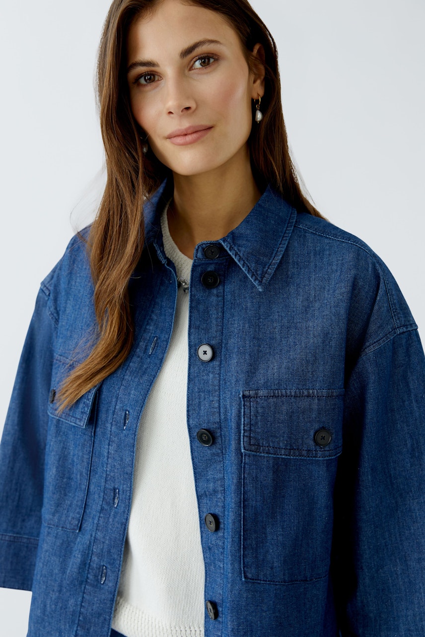 Lässige Damen-Jeansjacke: Frau mit blauer Jacke und hellem Pullover, lächelt freundlich in die Kamera.