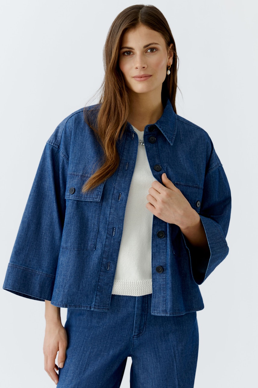 Damen-Jeansjacke: Frau in lässiger, blauer Jeansjacke mit weit geschnittenen Ärmeln und hellem Pullover.