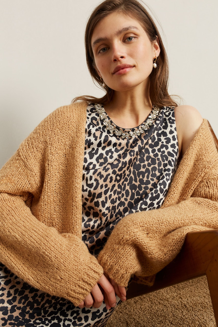 A-Linien-Kleid: Frau in einem Kleid mit Leopardenmuster, lässig und modern, kombiniert mit einem grob gestrickten Cardigan.