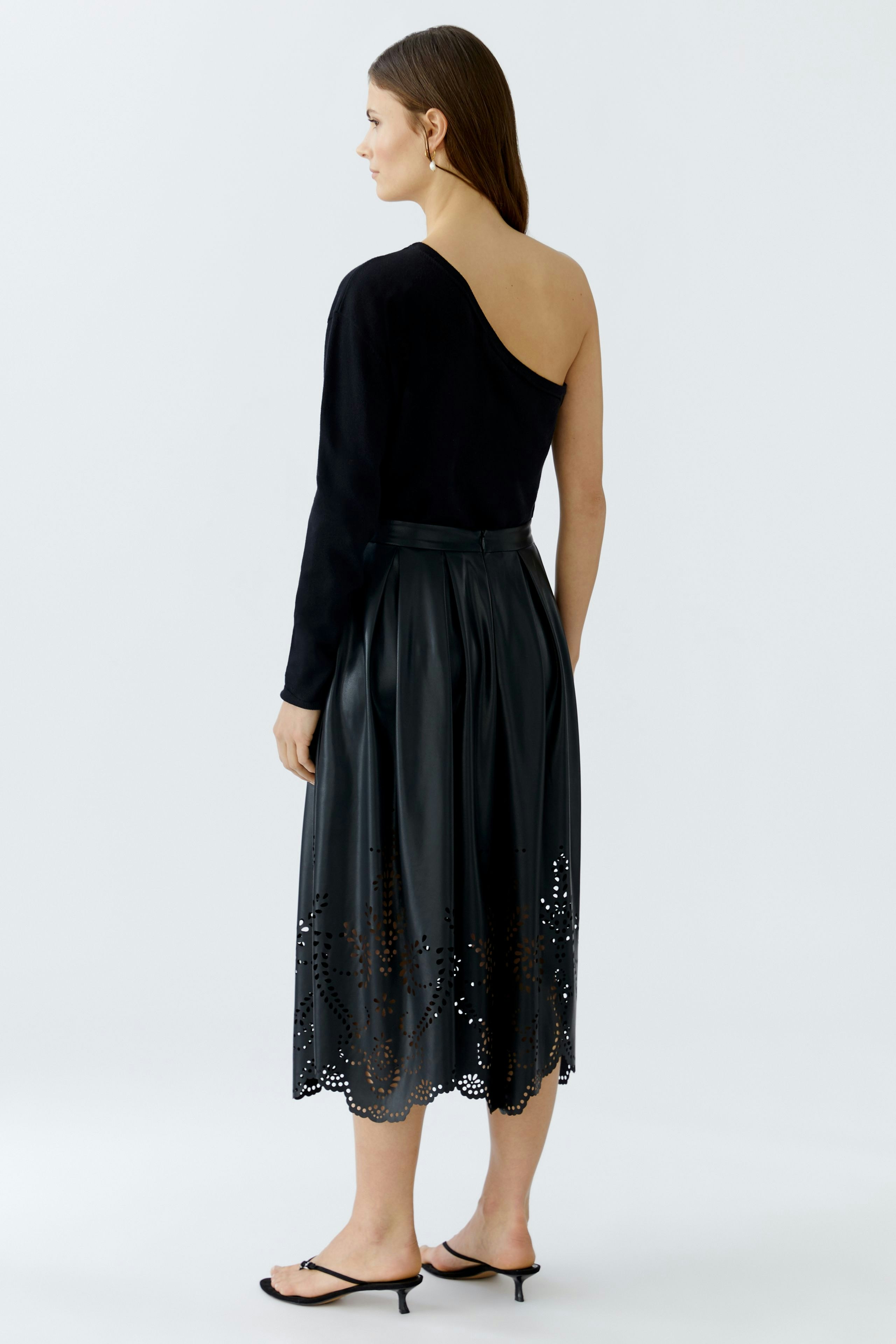 Damen-Lederimitatrock: Frau in schwarzem Rock mit Lochmuster und lässigem Oberteil von hinten.