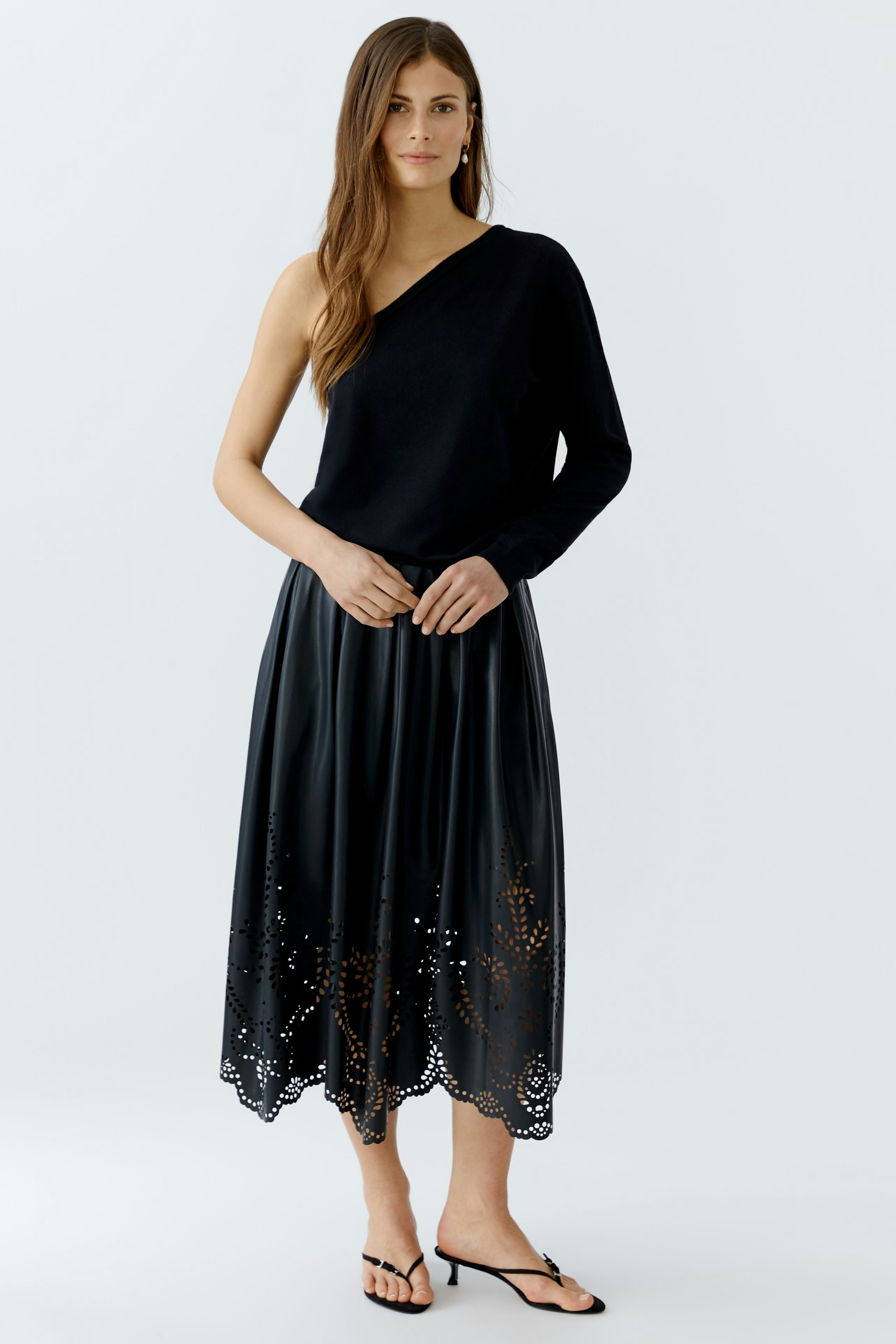 Damen-Lederimitatrock: Frau in schwarzem Rock mit filigranem Muster und lässigem Oberteil.