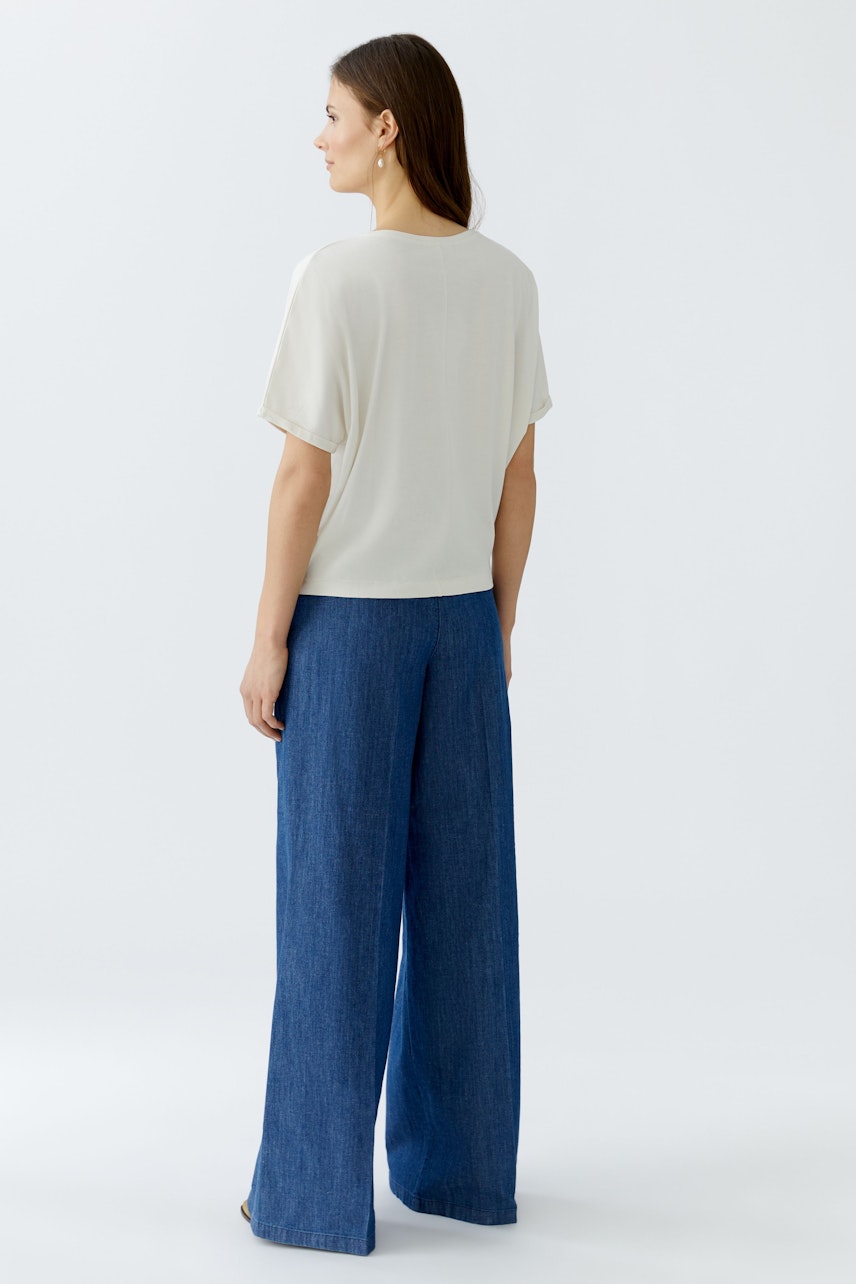 Bequeme Damen-T-Shirt: Frau trägt ein helles T-Shirt mit lockerer Passform und weiten Jeans.
