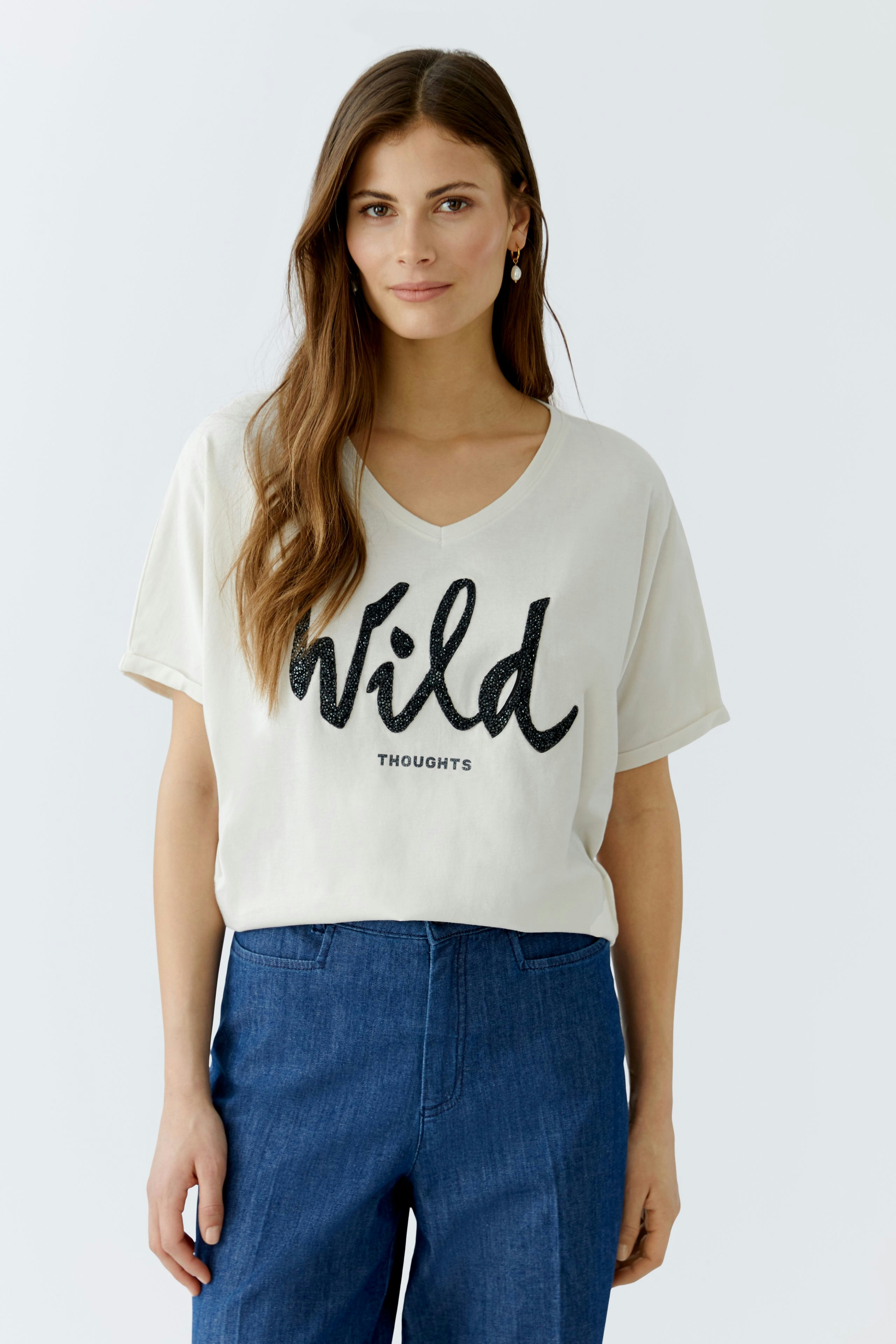 Casual women's T-shirt: Young woman in a light top with 'Wild Thoughts' print, paired with blue pants.