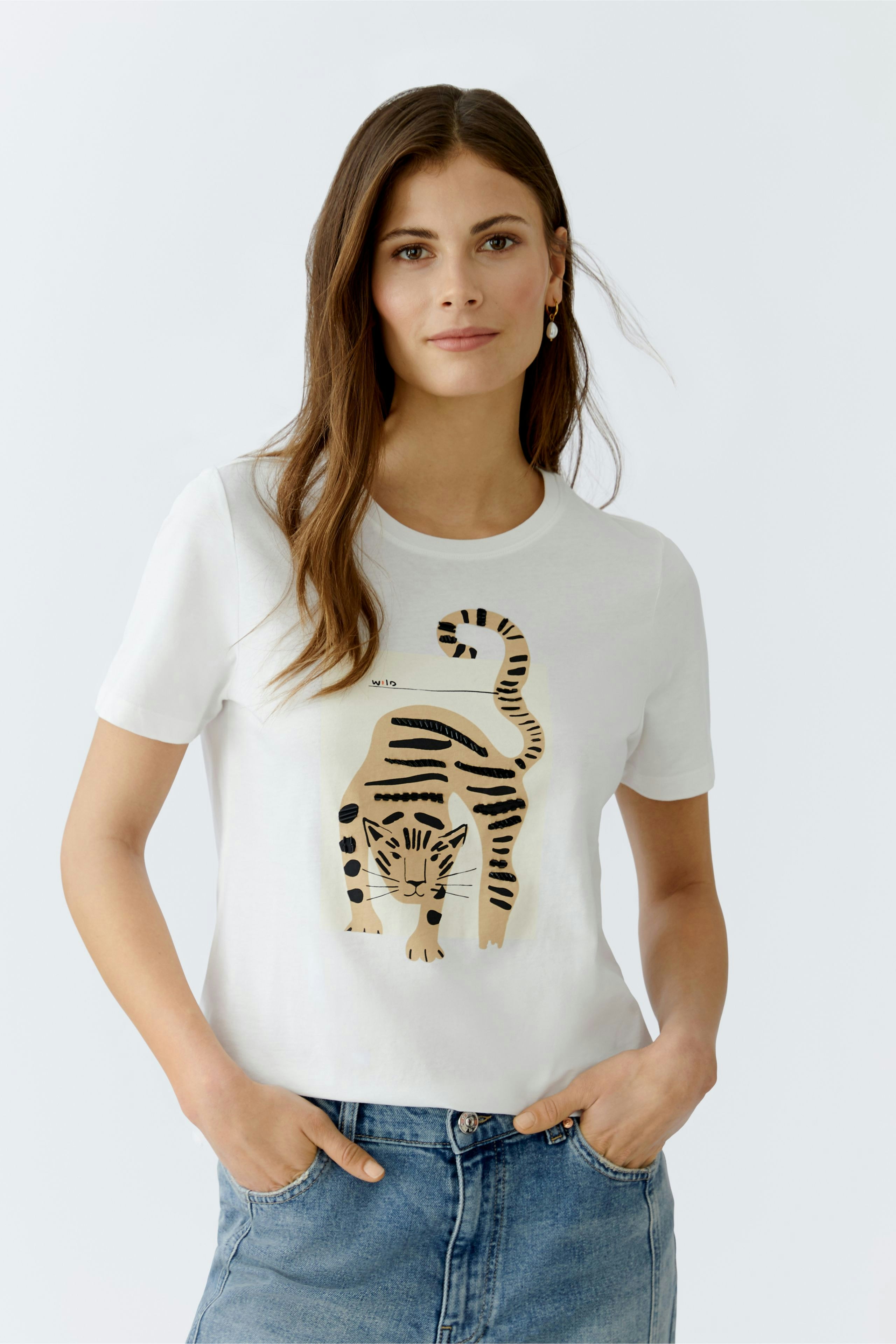Casual women's T-shirt: Young woman in a white tee featuring a tiger graphic, paired with denim.