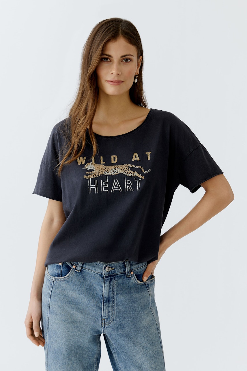 Bequeme Damen-T-Shirt: Frau trägt ein schwarzes Shirt mit Leopardenmotiv und lässigem Schnitt.