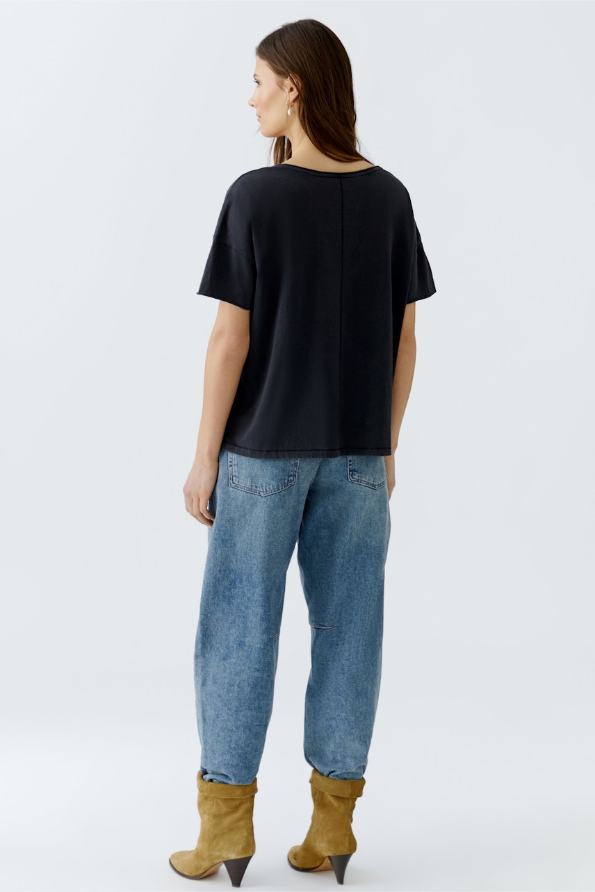 Bequemer Damen-T-Shirt: Frau in schwarzem T-Shirt mit lässigem Schnitt und lockeren Jeans von hinten.