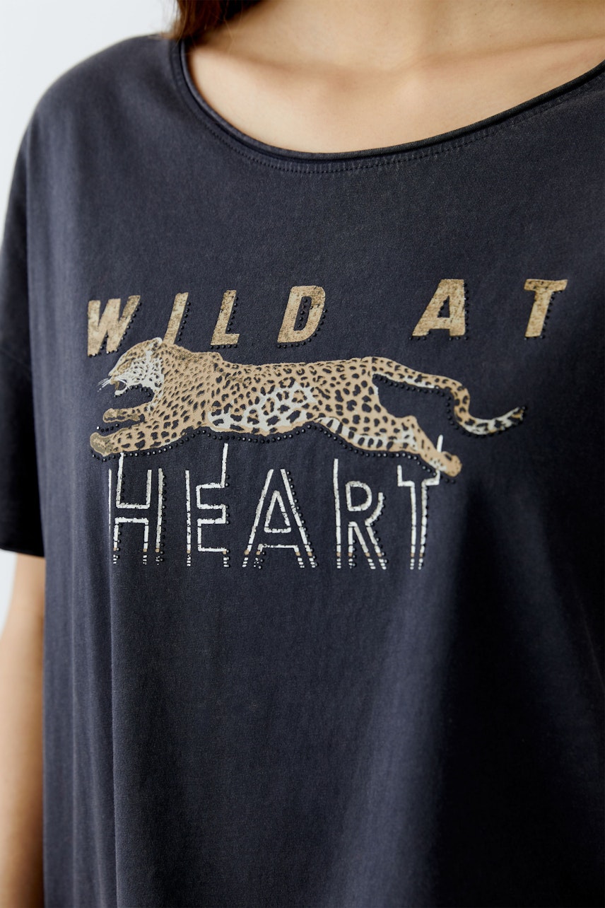 Bequemes Damen-T-Shirt: Frau trägt ein schwarzes Shirt mit Leopardenmotiv und auffälligem Schriftzug.
