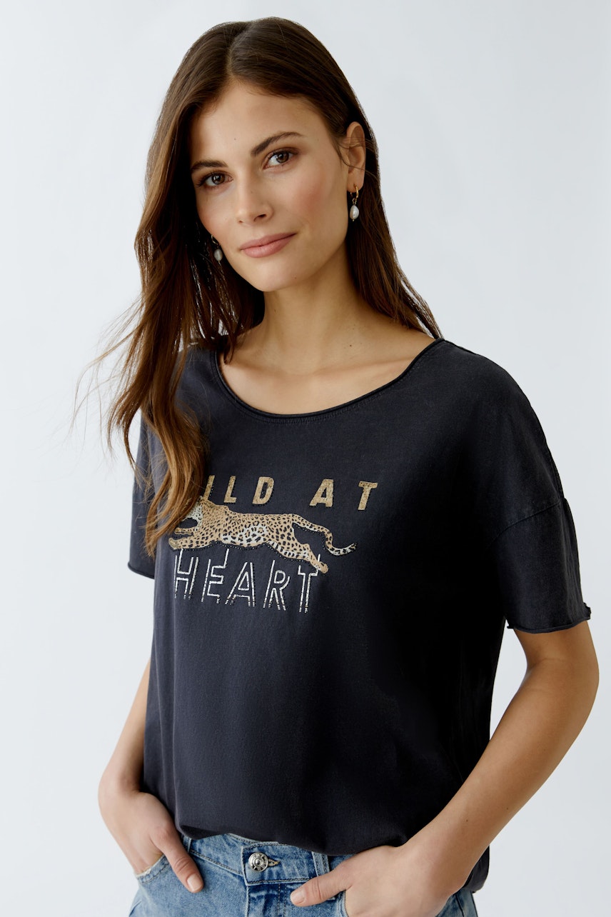 Bequemes Damen-T-Shirt: Junge Frau trägt ein schwarzes T-Shirt mit goldfarbenem Aufdruck und lässigem Schnitt.
