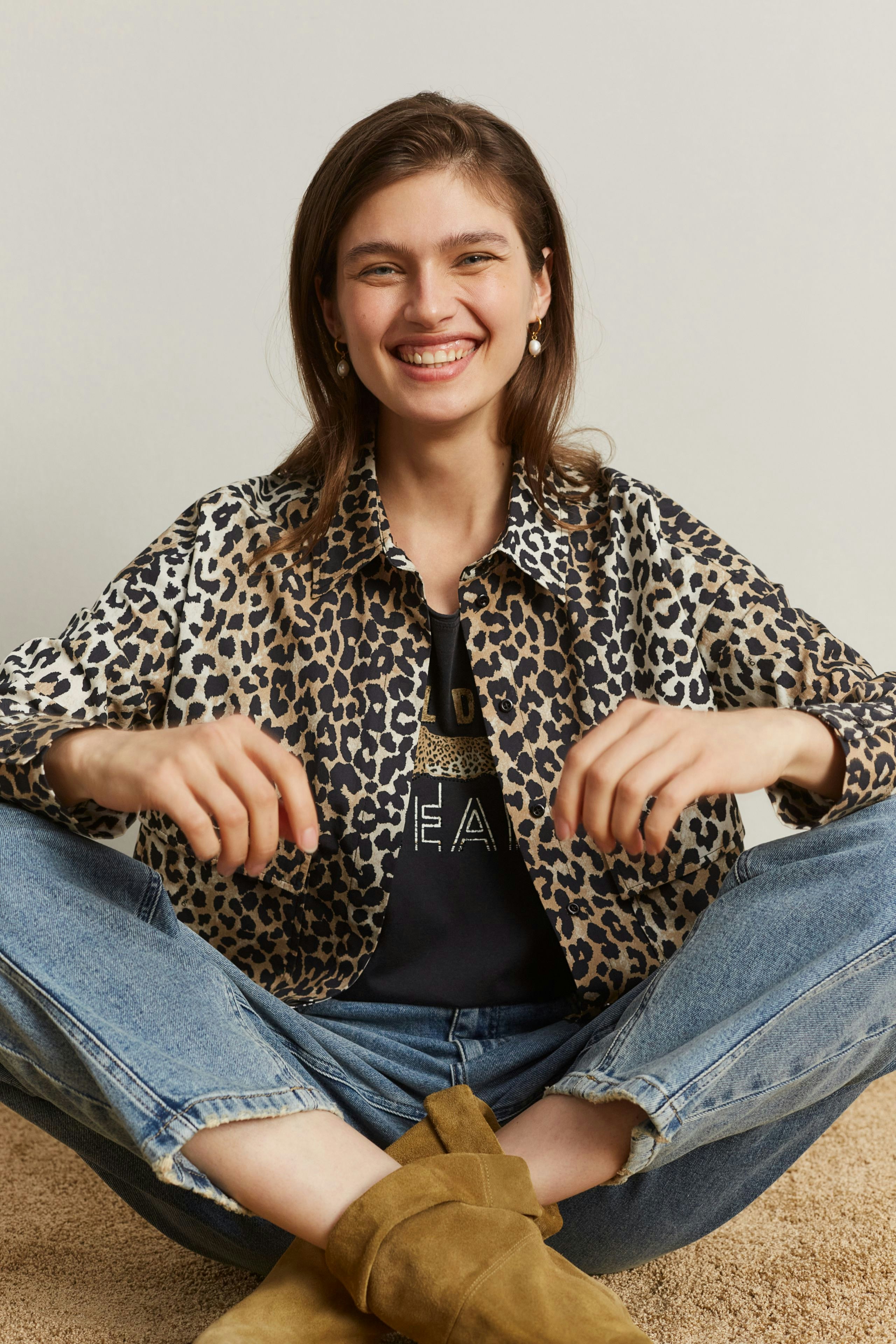 Casual women's T-shirt: Smiling woman in a leopard print shirt over a graphic tee, sitting comfortably.