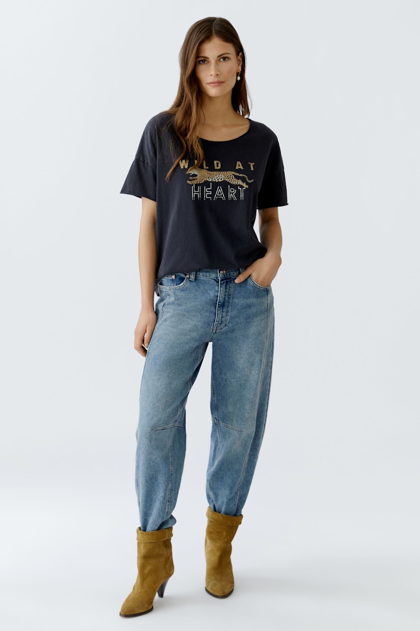 Damen-T-Shirt: Junge Frau trägt ein schwarzes T-Shirt mit goldenen Buchstaben und lässigen Jeans.