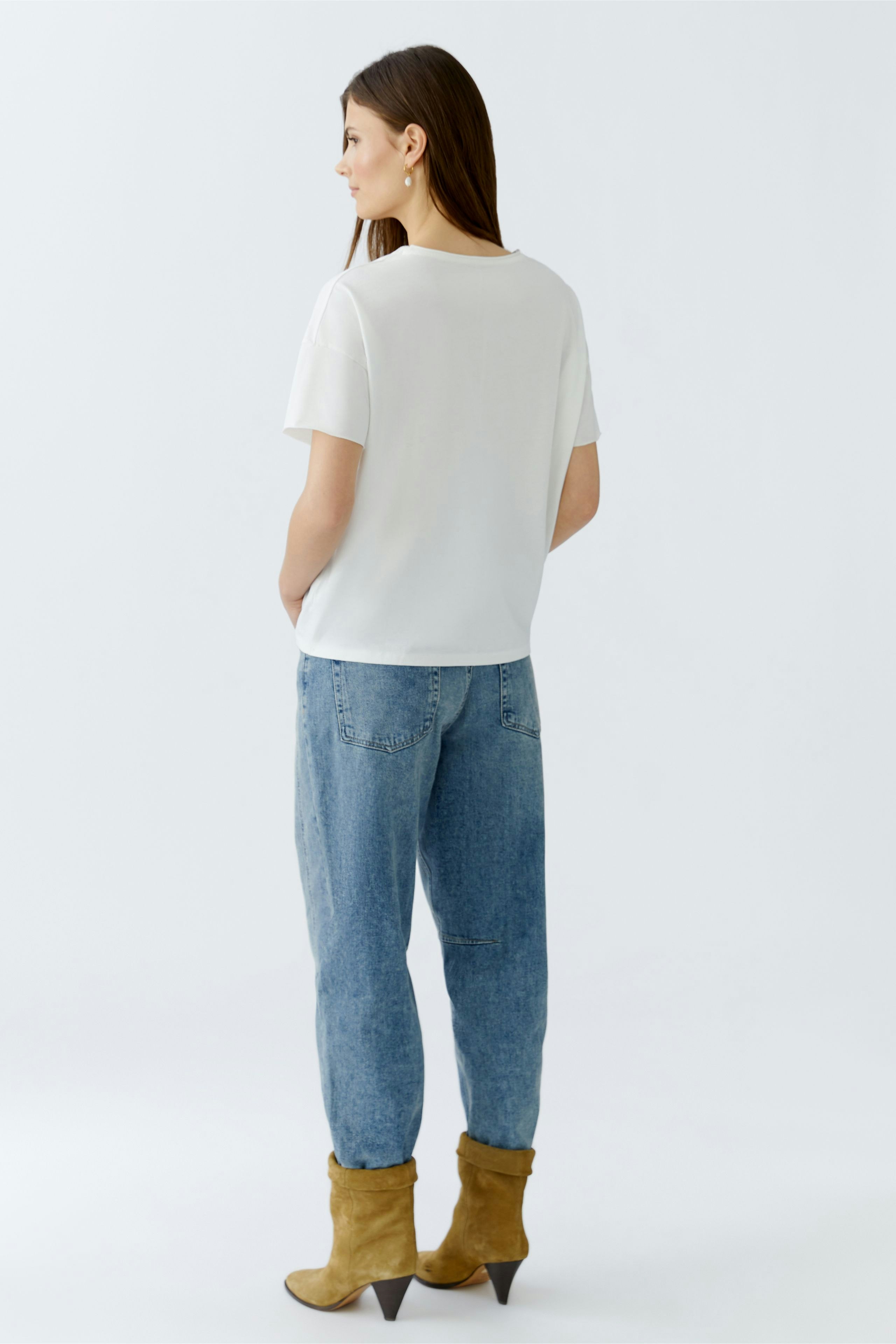 Casual women's T-shirt: Young woman in a white short-sleeve top paired with relaxed-fit jeans.