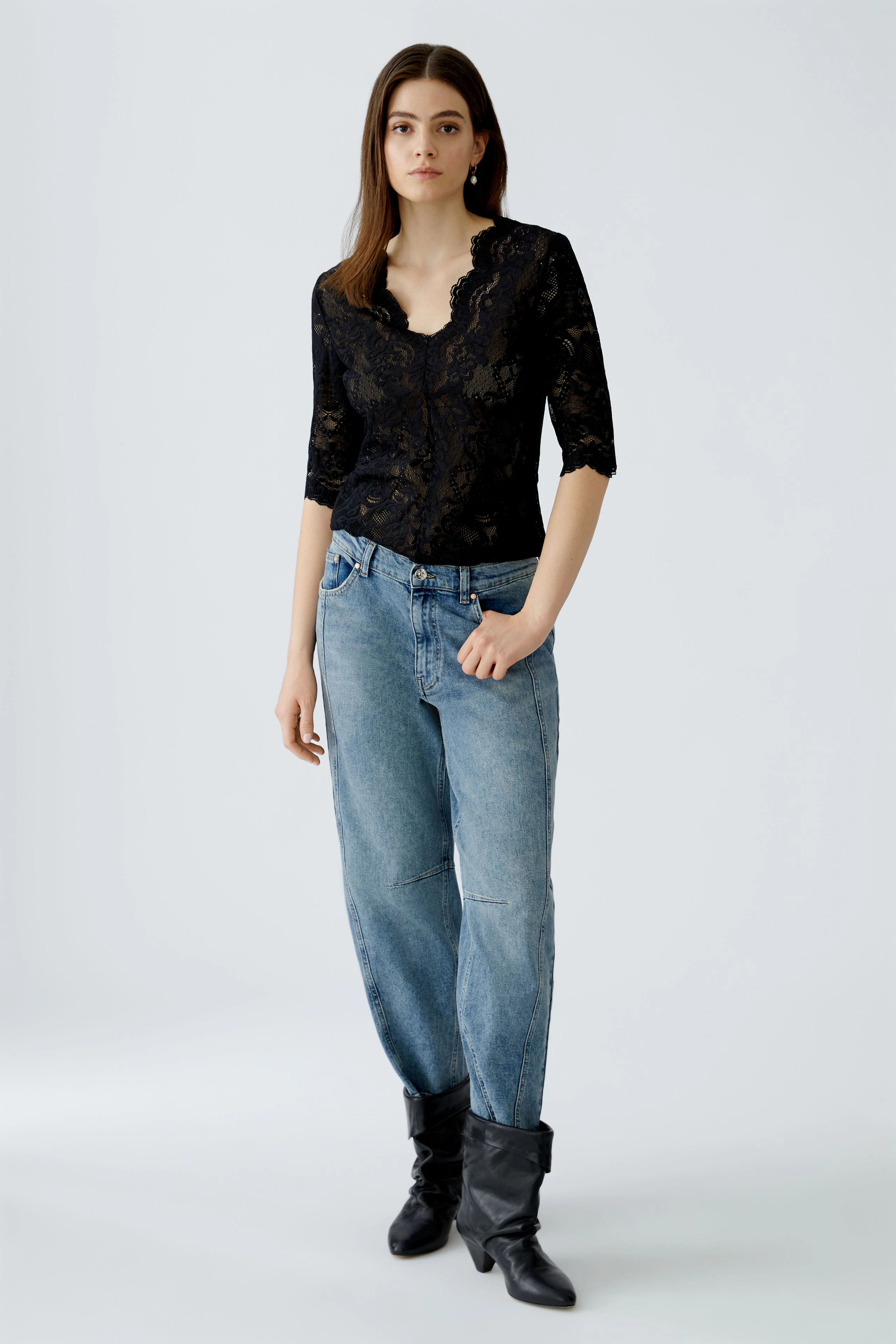 Damen-T-Shirt: Frau in schwarzem, leicht transparentem T-Shirt mit Spitzenmuster und lässigen Jeans.