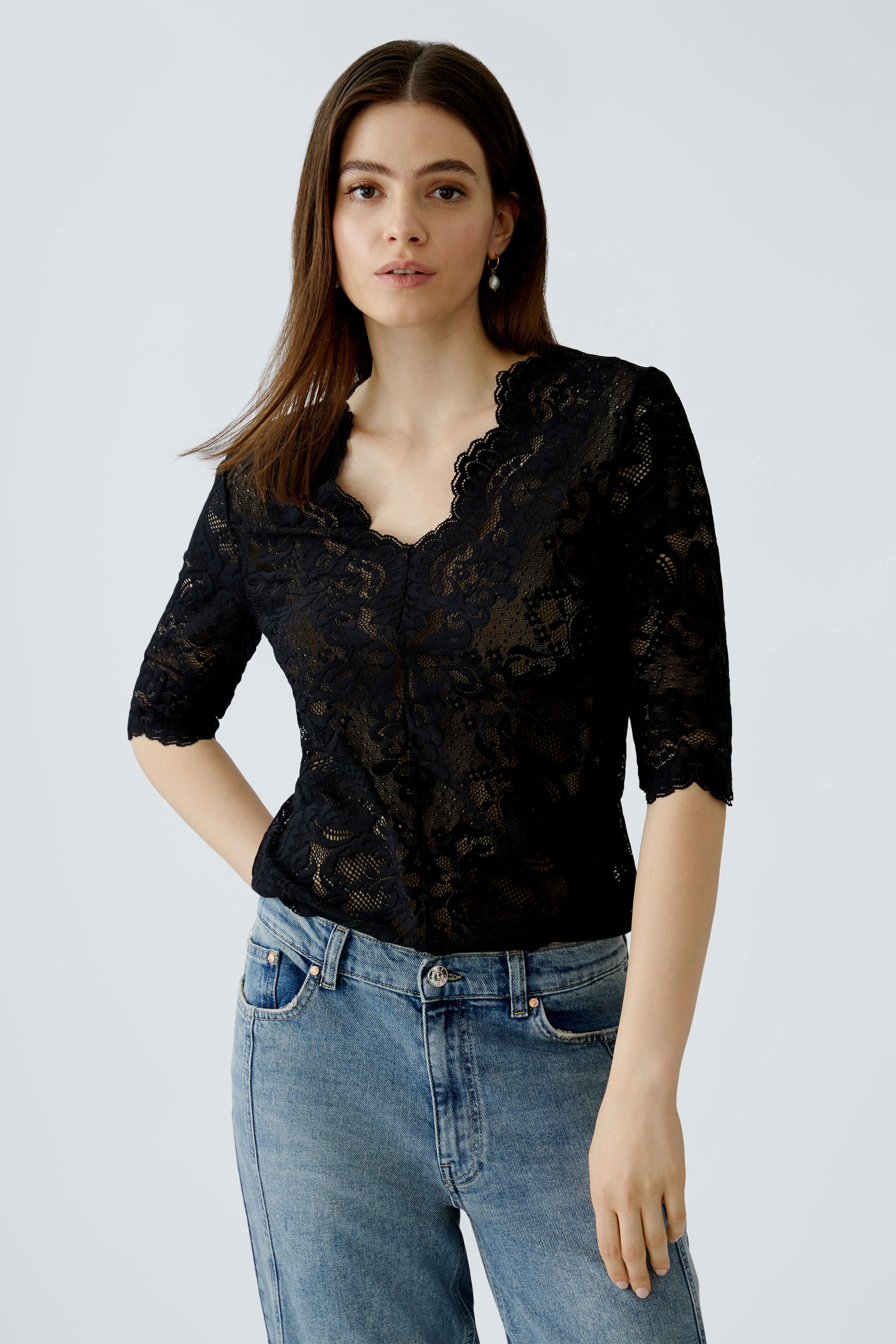 Schwarzes Damen-T-Shirt aus Spitze mit V-Ausschnitt und 3/4-Ärmeln, lässig kombiniert mit Jeans.