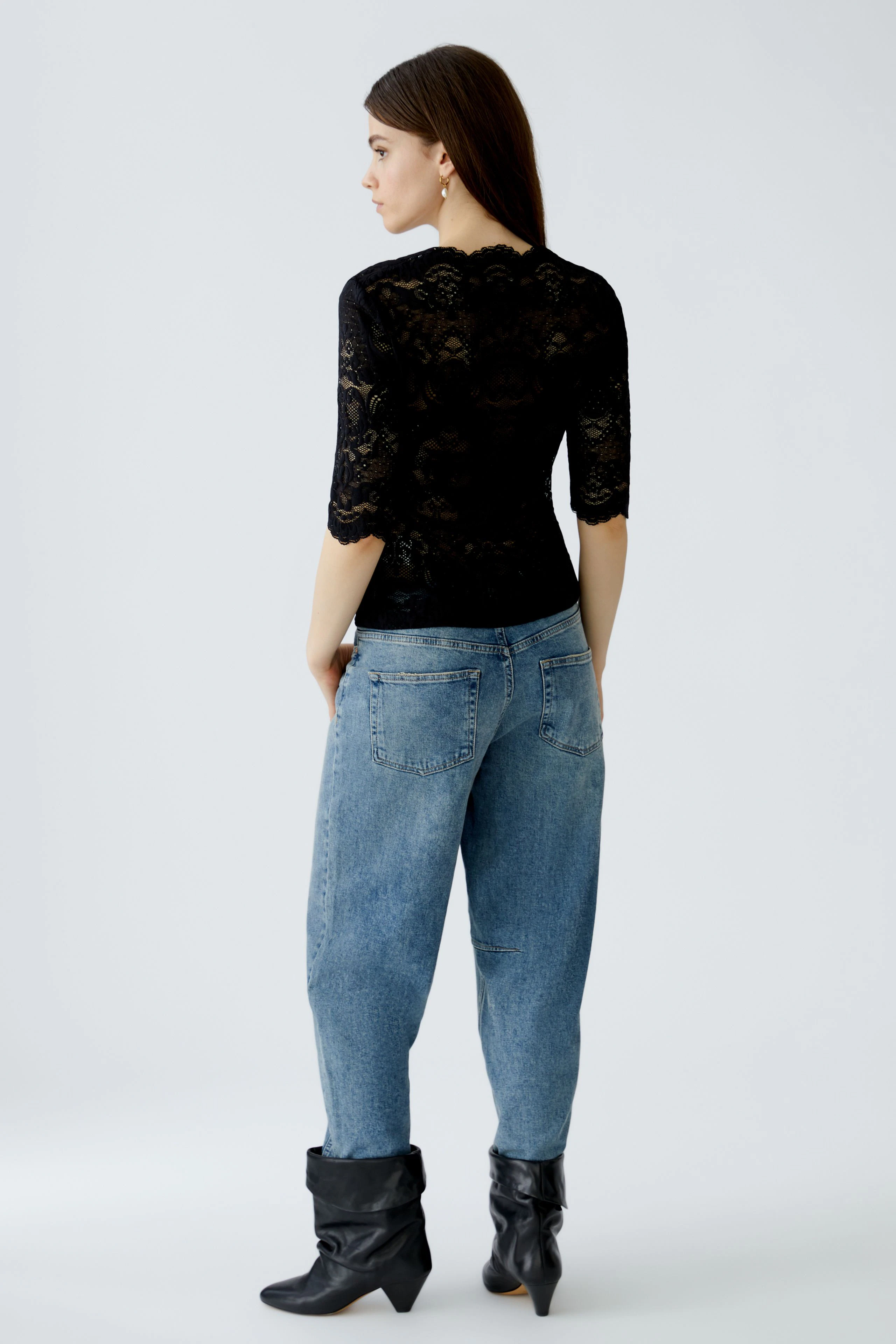 Damen-T-Shirt: Frau in schwarzem, transparentem T-Shirt mit Spitzenmuster und lässigen Jeans.