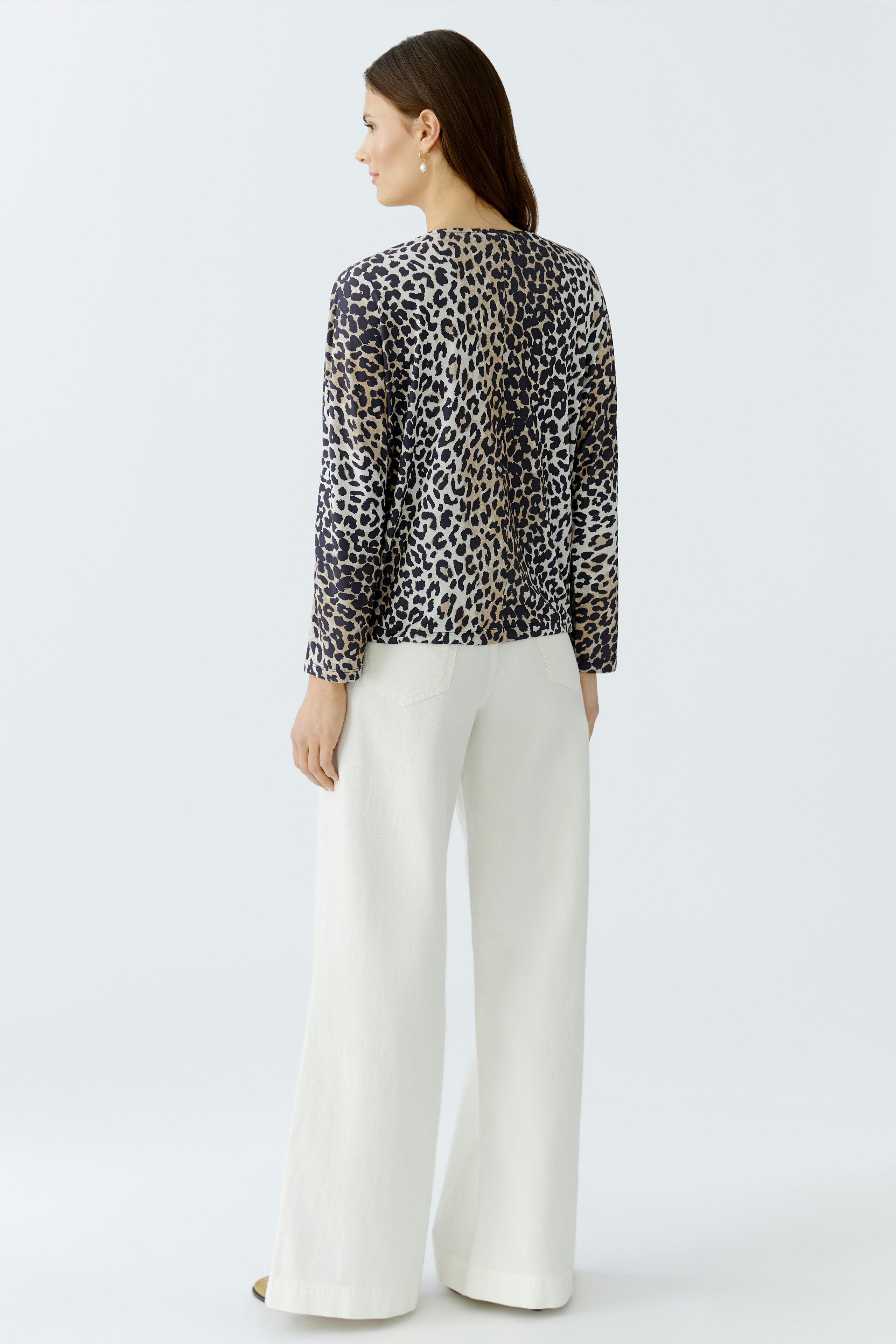 Casual women's blouse: Woman in a leopard print blouse and white wide-leg pants, viewed from the back.
