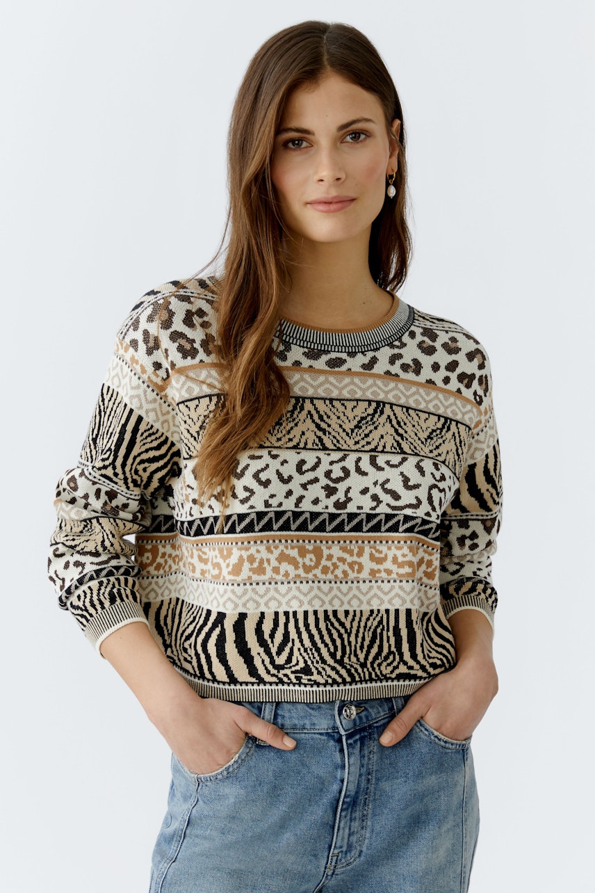 Damen-Pullover: Frau trägt einen gemusterten Pullover mit verschiedenen Tiermotiven und lässigen Jeans.