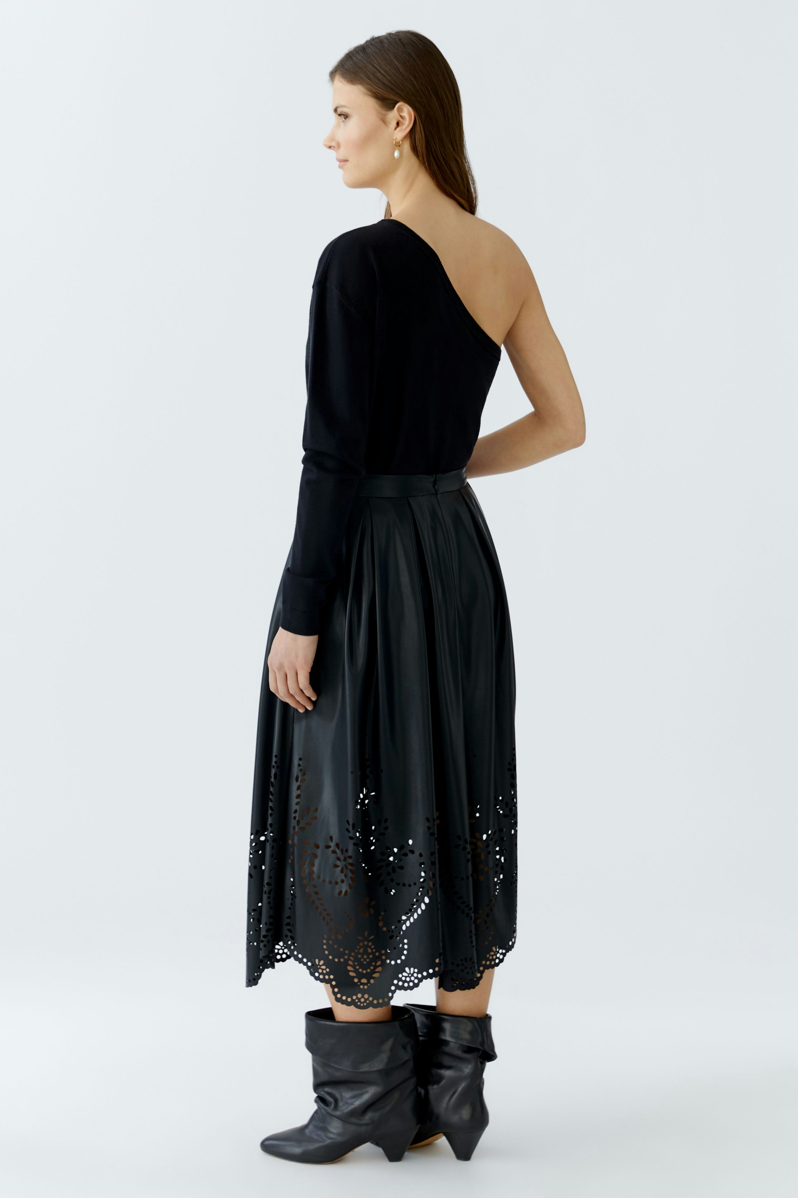 Damen-Pullover: Frau in schwarzem Pullover mit asymmetrischem Schnitt und schwarzem Rock im Hintergrund.