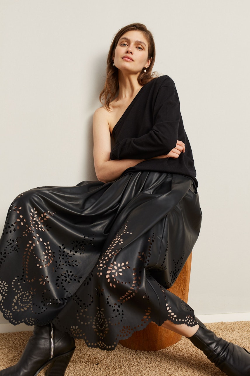 Casual women's pullover: Woman in a black pullover paired with a stylish skirt, sitting confidently.
