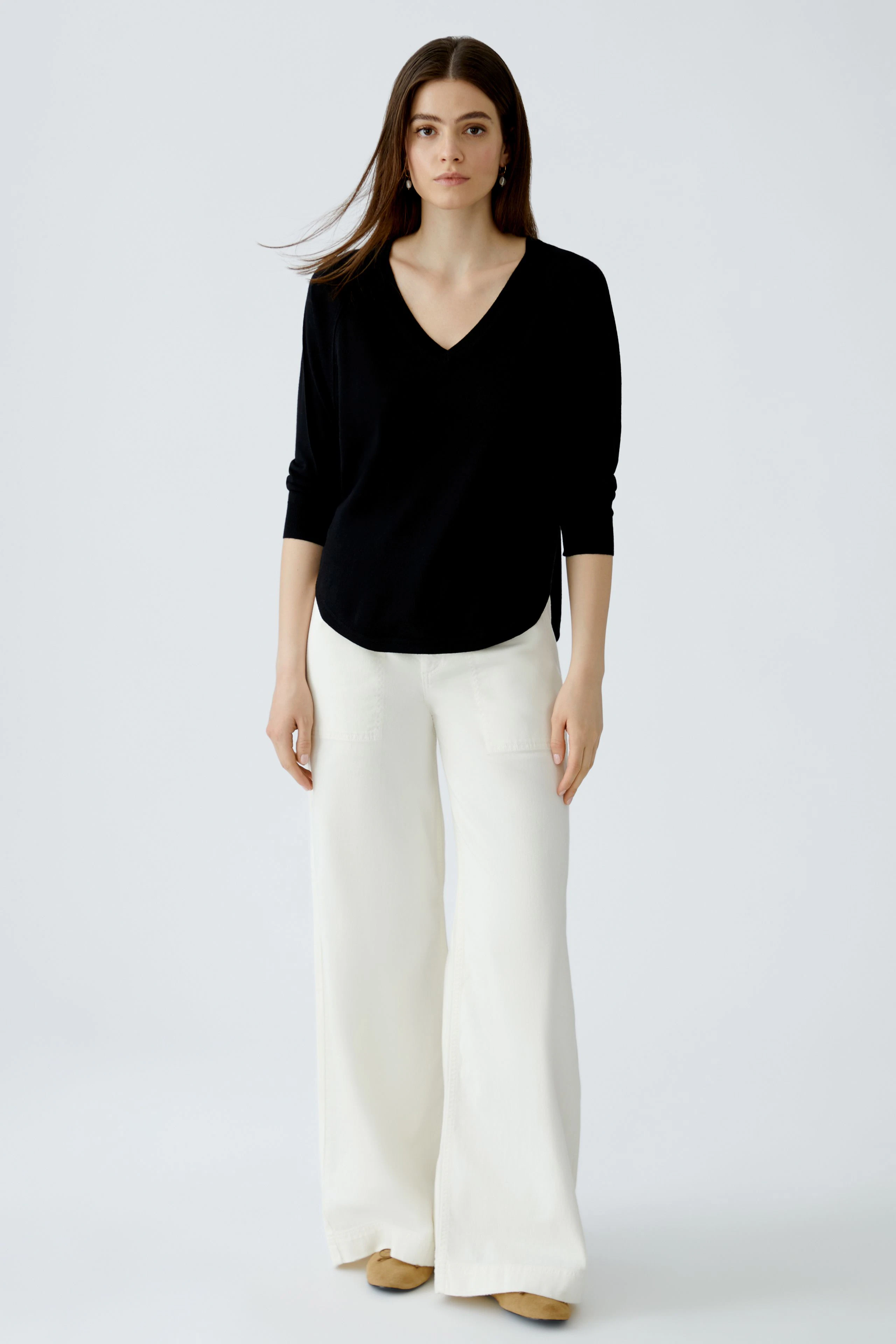 Schwarzer Damen-Pullover mit V-Ausschnitt, lässig kombiniert mit weißen, weiten Hosen.