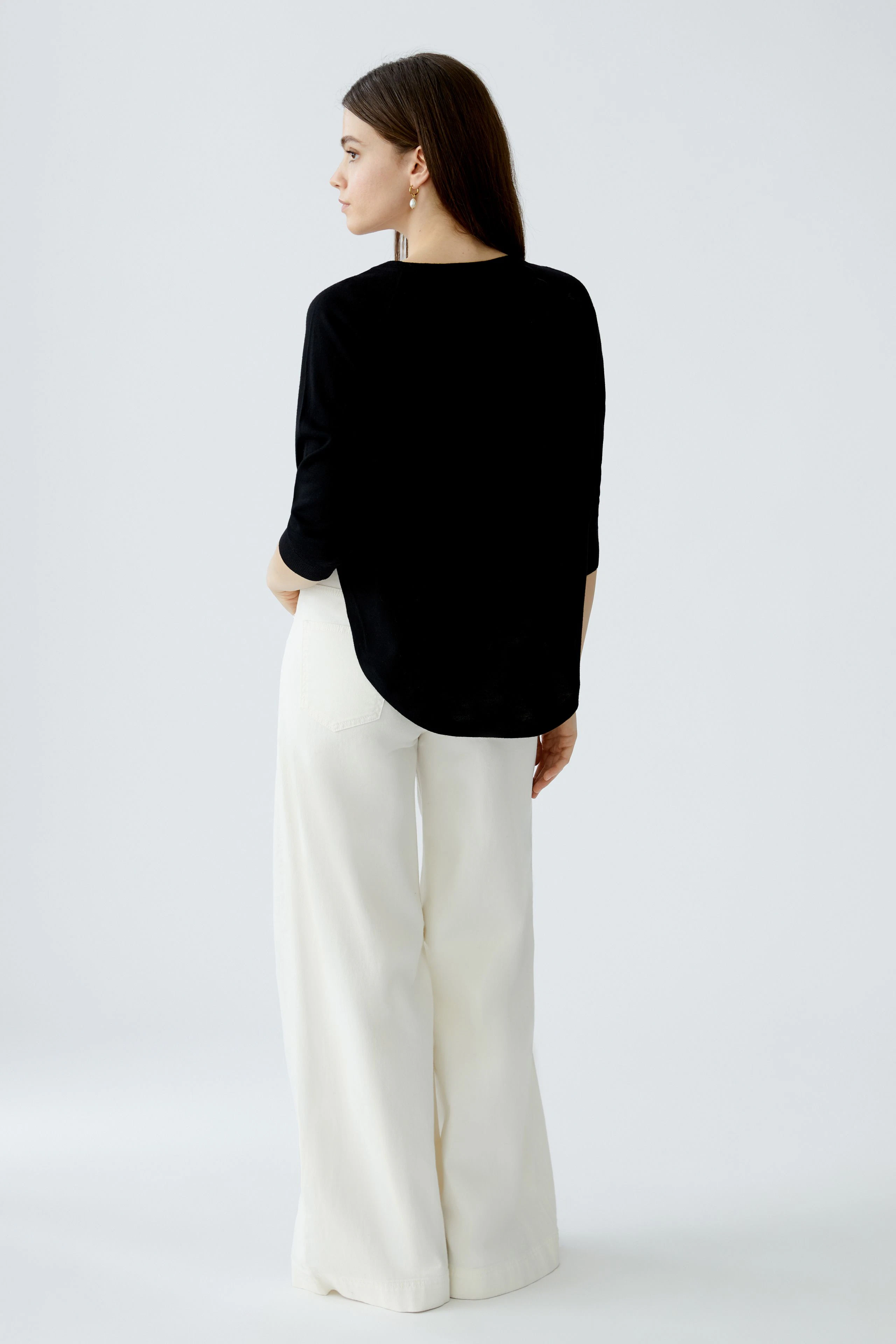 Damen-Pullover: Frau trägt einen schwarzen Pullover mit lässigem Schnitt und weißen Hosen.