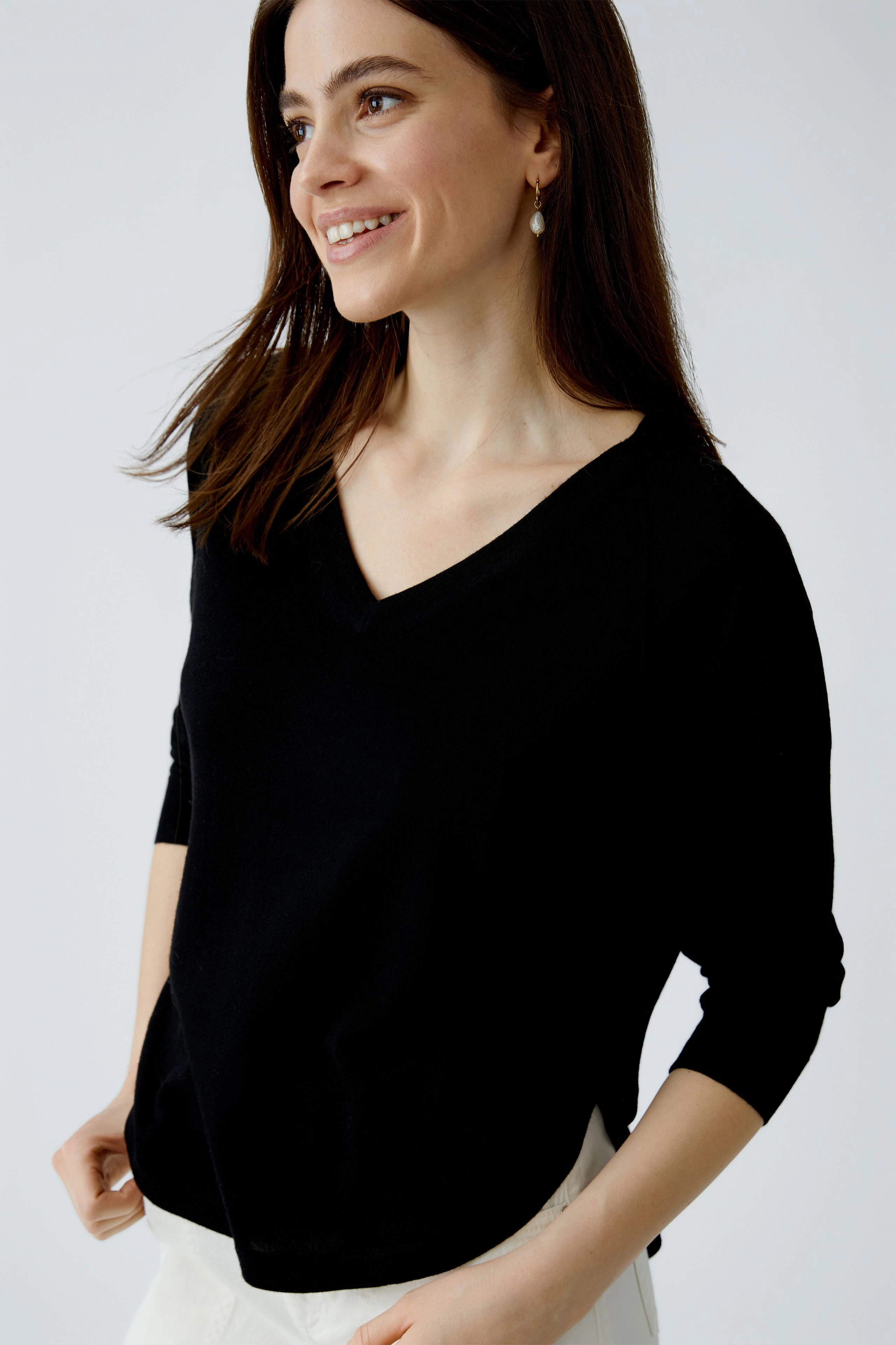 Damen-Pullover: Junge Frau in schwarzem V-Pullover mit lässigem Schnitt und fröhlichem Lächeln.