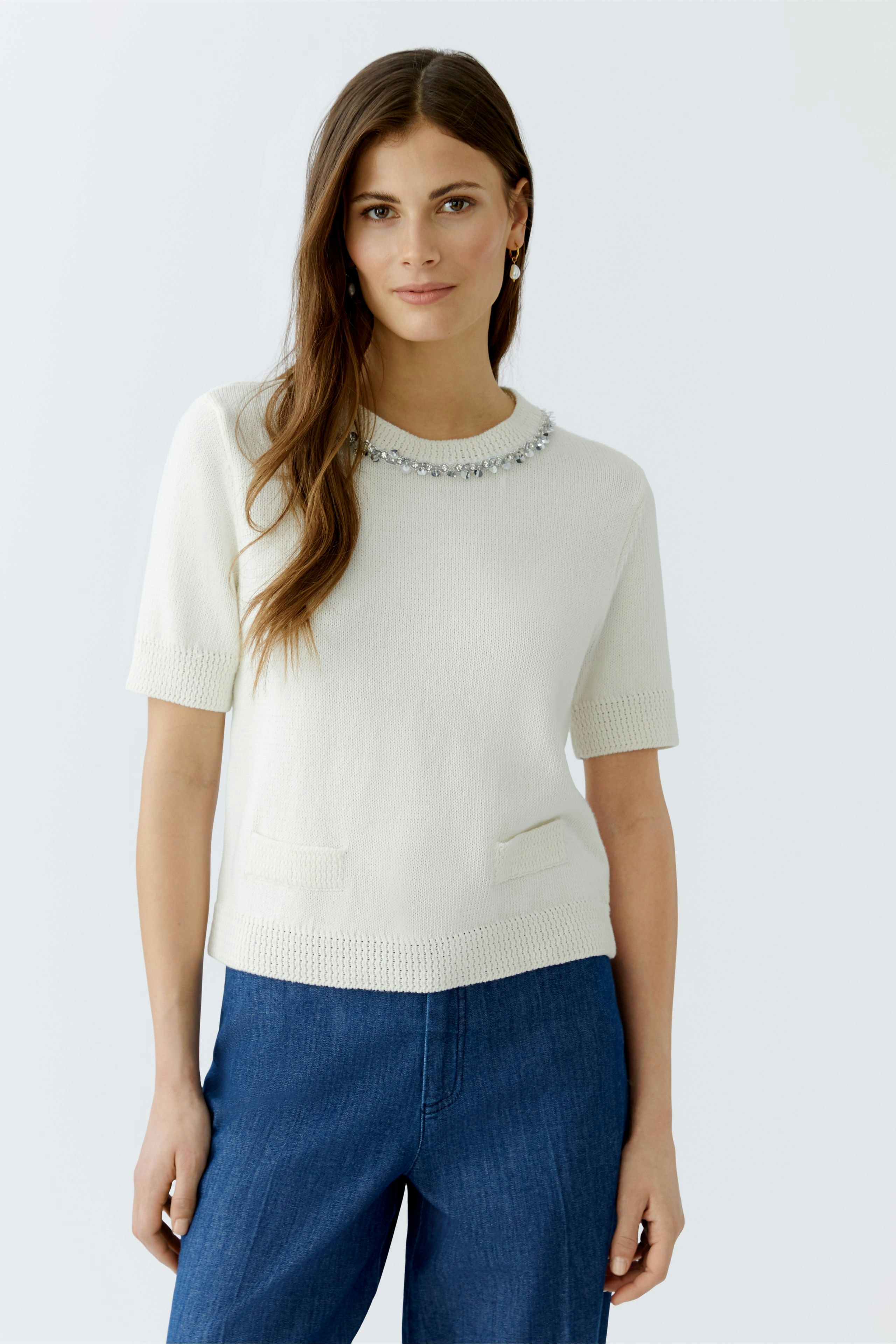 Damen-Pullover: Frau in hellem Pullover mit Schmuckdetails und kurzen Ärmeln, kombiniert mit lässiger Hose.
