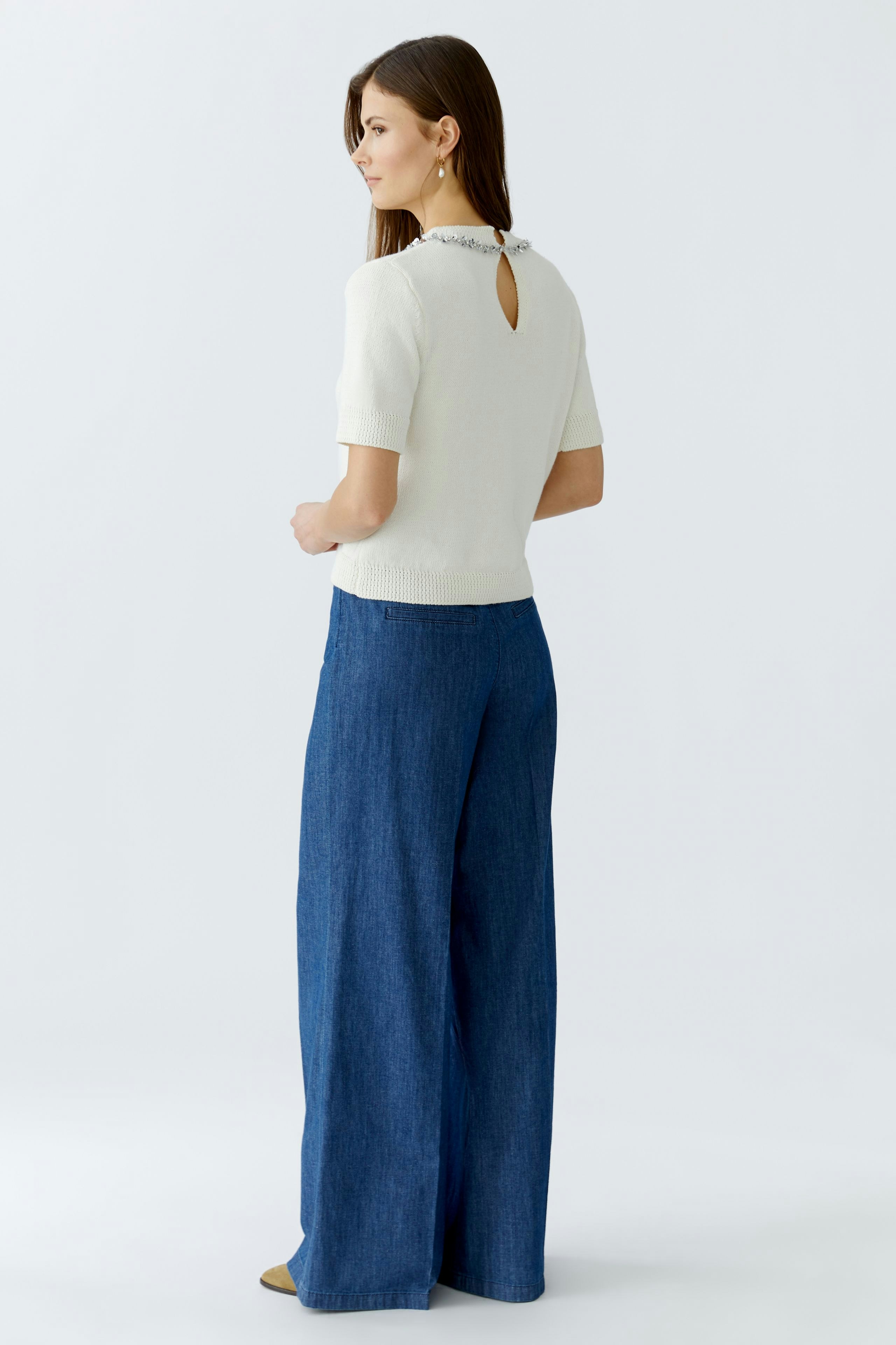 Damen-Pullover: Frau in weißem Pullover mit Rückenausschnitt und blauen, weiten Jeans.