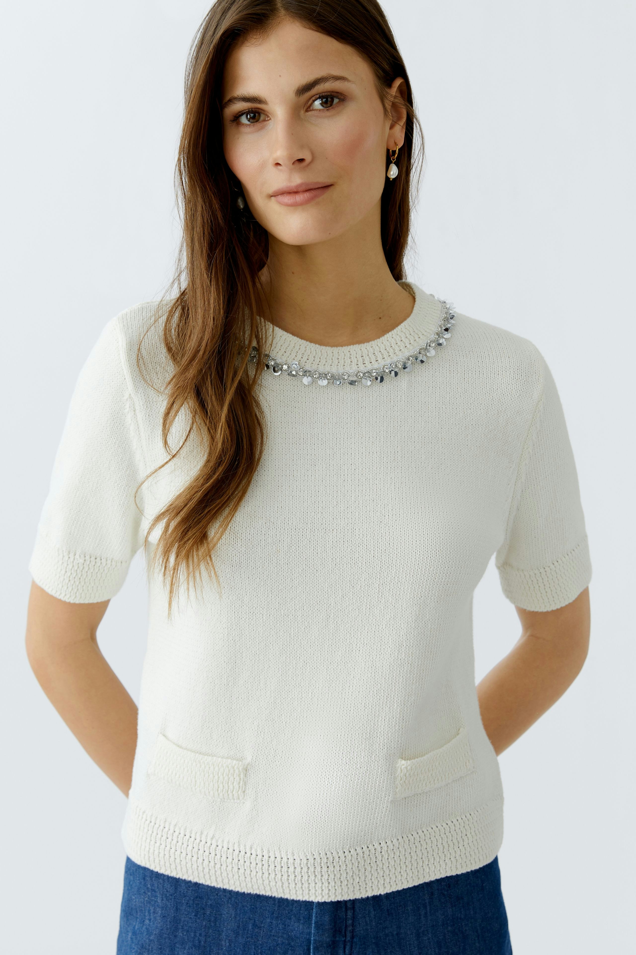 Damen-Pullover: Frau in weißem Pullover mit Schmuckkragen und Taschen, lässig und modern.