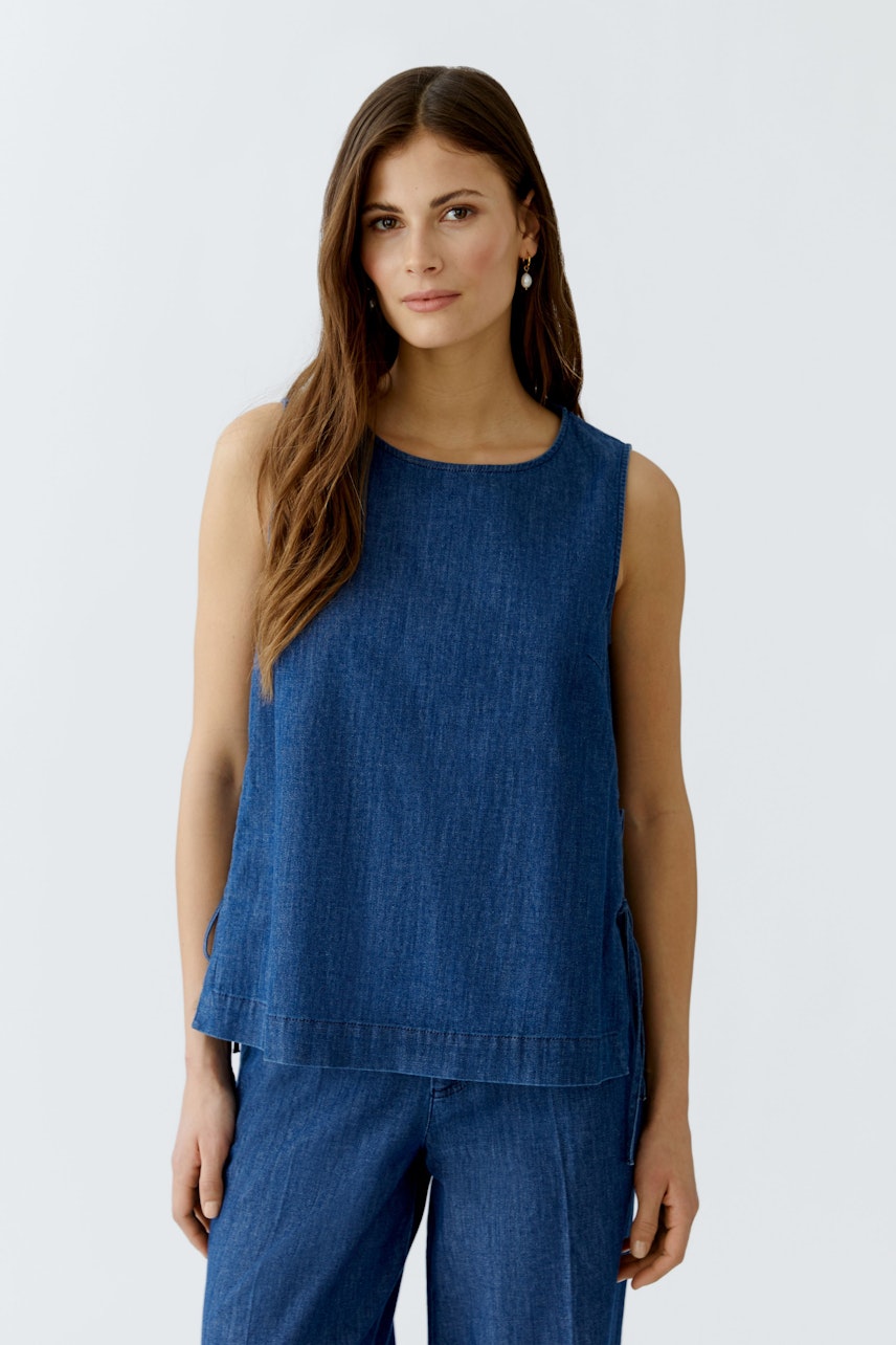 Bequeme Damen-Top: Frau trägt ein ärmelloses, blaues Denim-Top mit lässigem Schnitt.