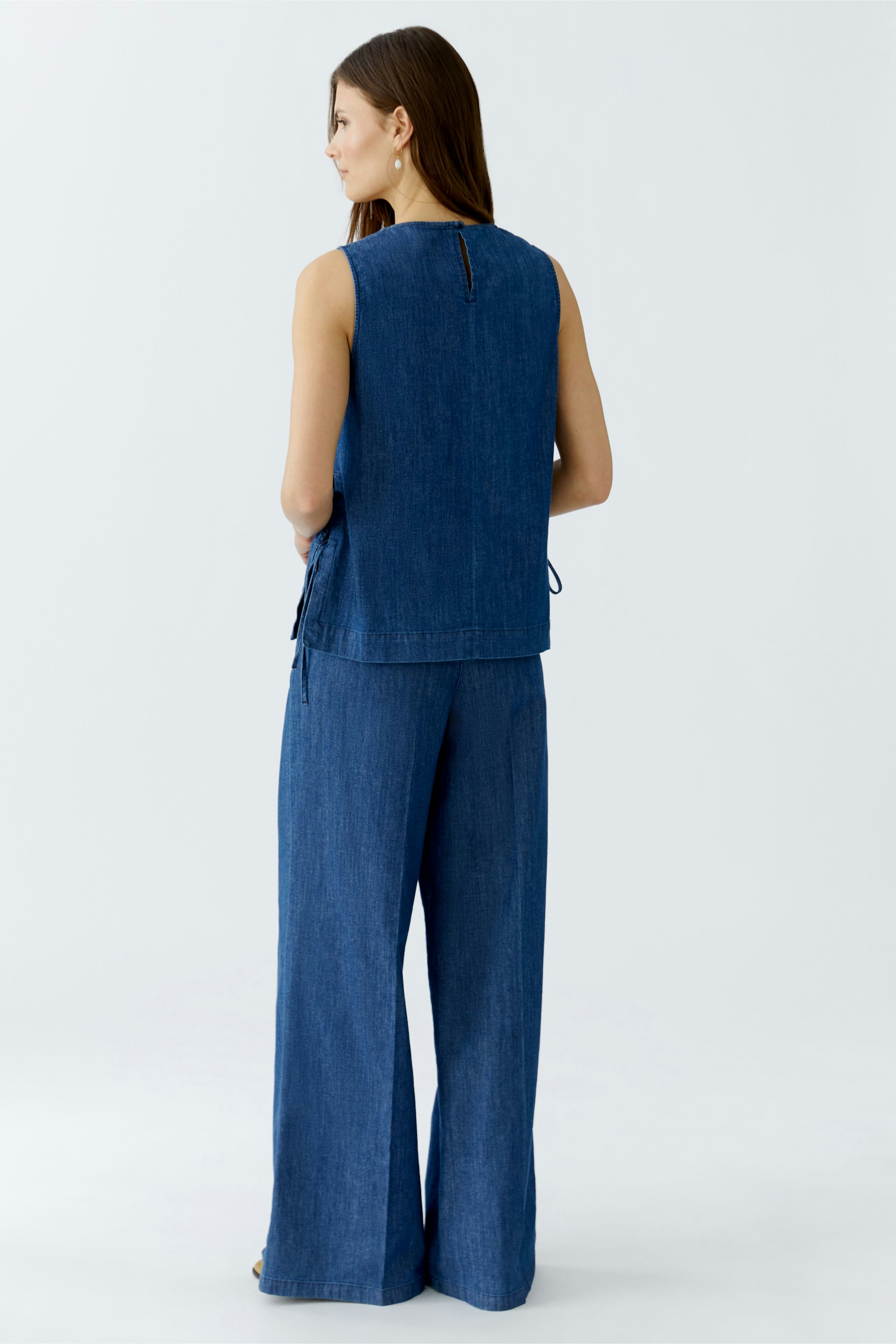 Casual women's top: A woman in a blue sleeveless top paired with wide-leg pants, showcasing a relaxed style.
