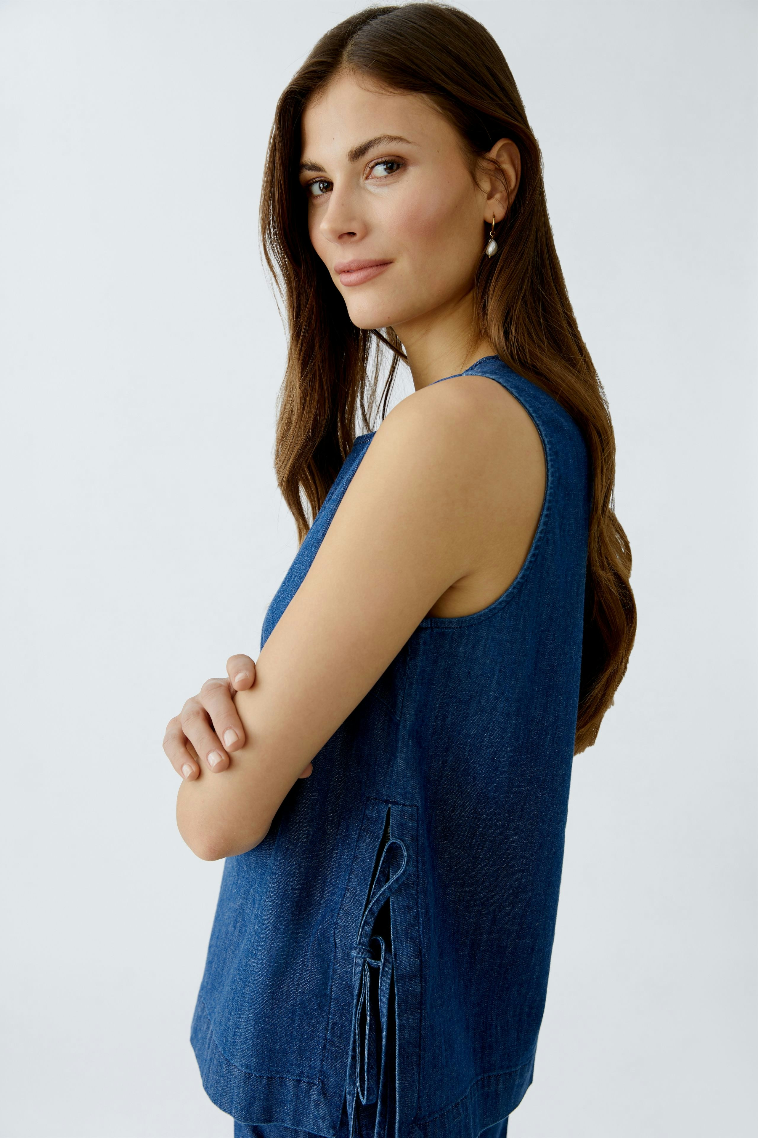 Casual women's top: Young woman in a blue sleeveless top with side ties, smiling confidently.