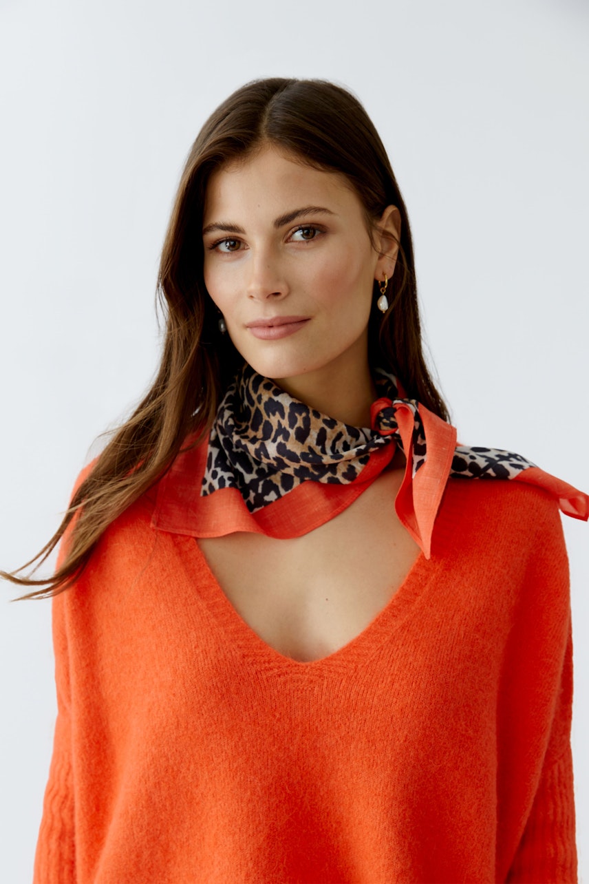 Vibrant scarf: Woman wearing a colorful scarf with a leopard print, styled with a cozy pullover.