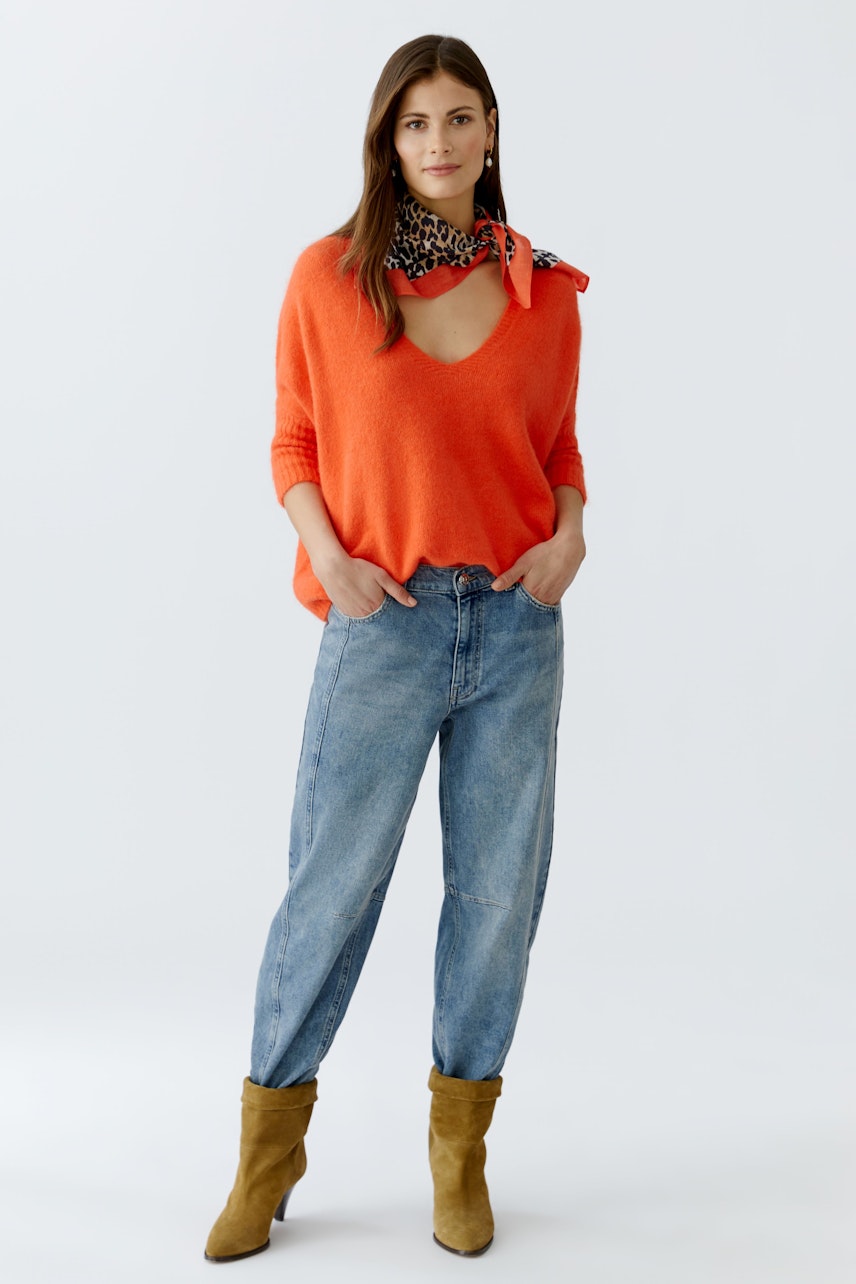 Casual scarf: Woman in a vibrant orange scarf tied around her neck, paired with a relaxed outfit.