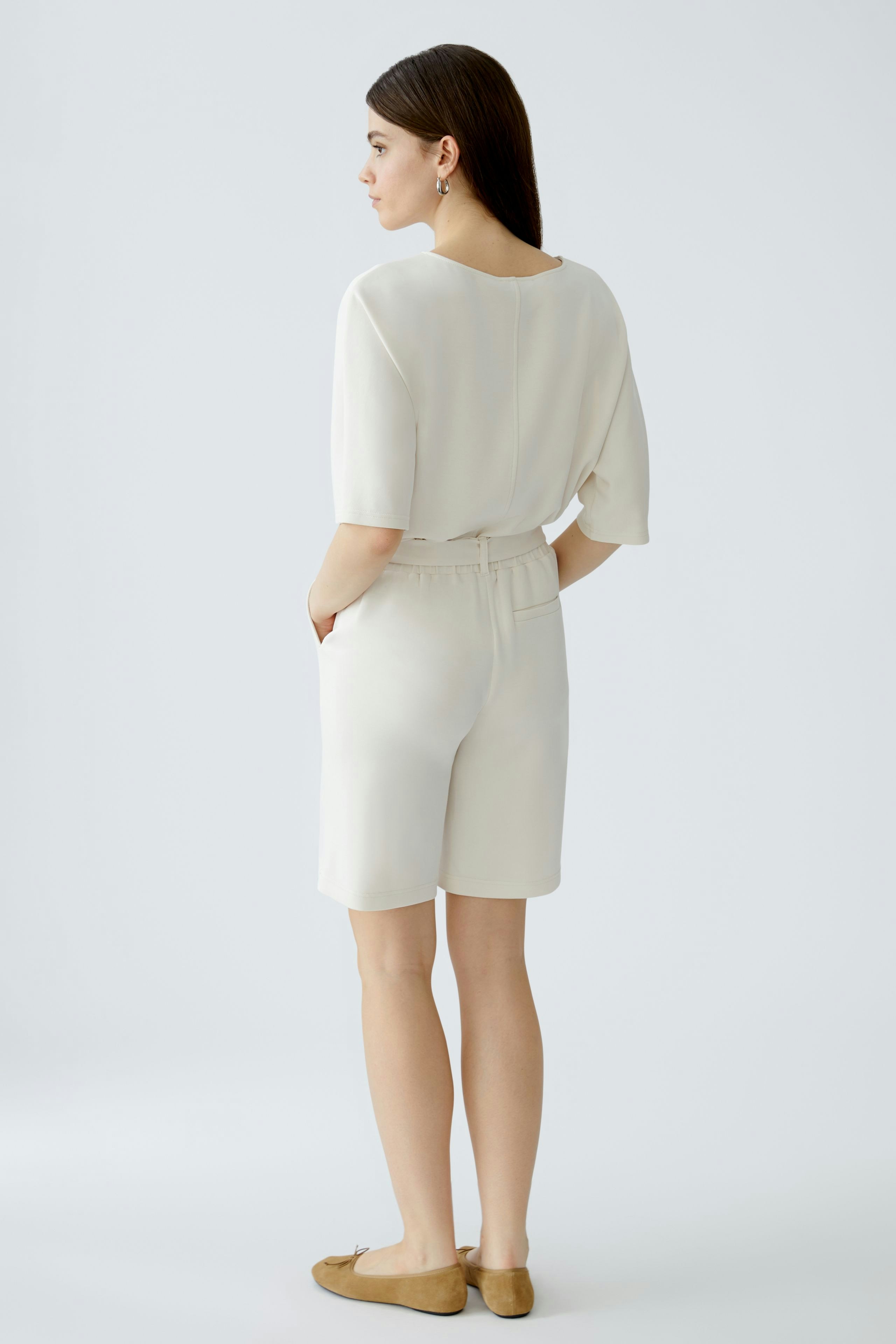 Bequeme Damen-Bermuda: Frau in hellen Shorts mit lässigem Oberteil und flachen Schuhen von hinten.