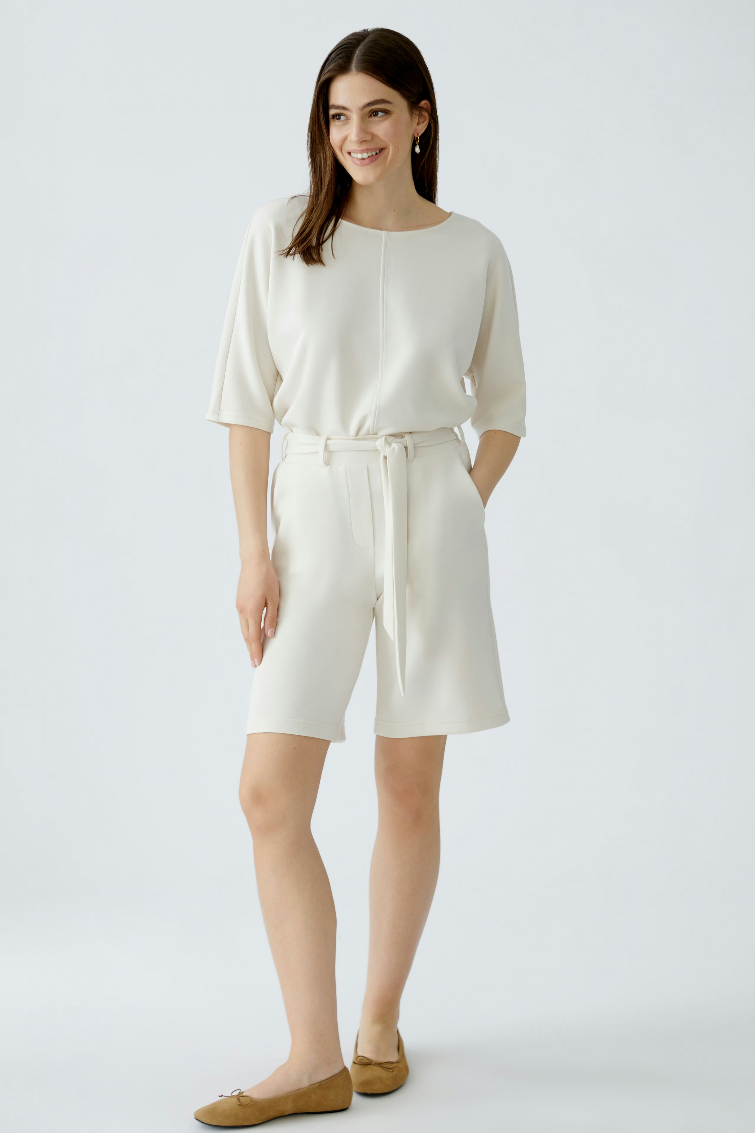 Modische Damen-Bermuda: Frau in beiger Bermuda mit Gürtel und lässigem Oberteil, strahlt Selbstbewusstsein aus.